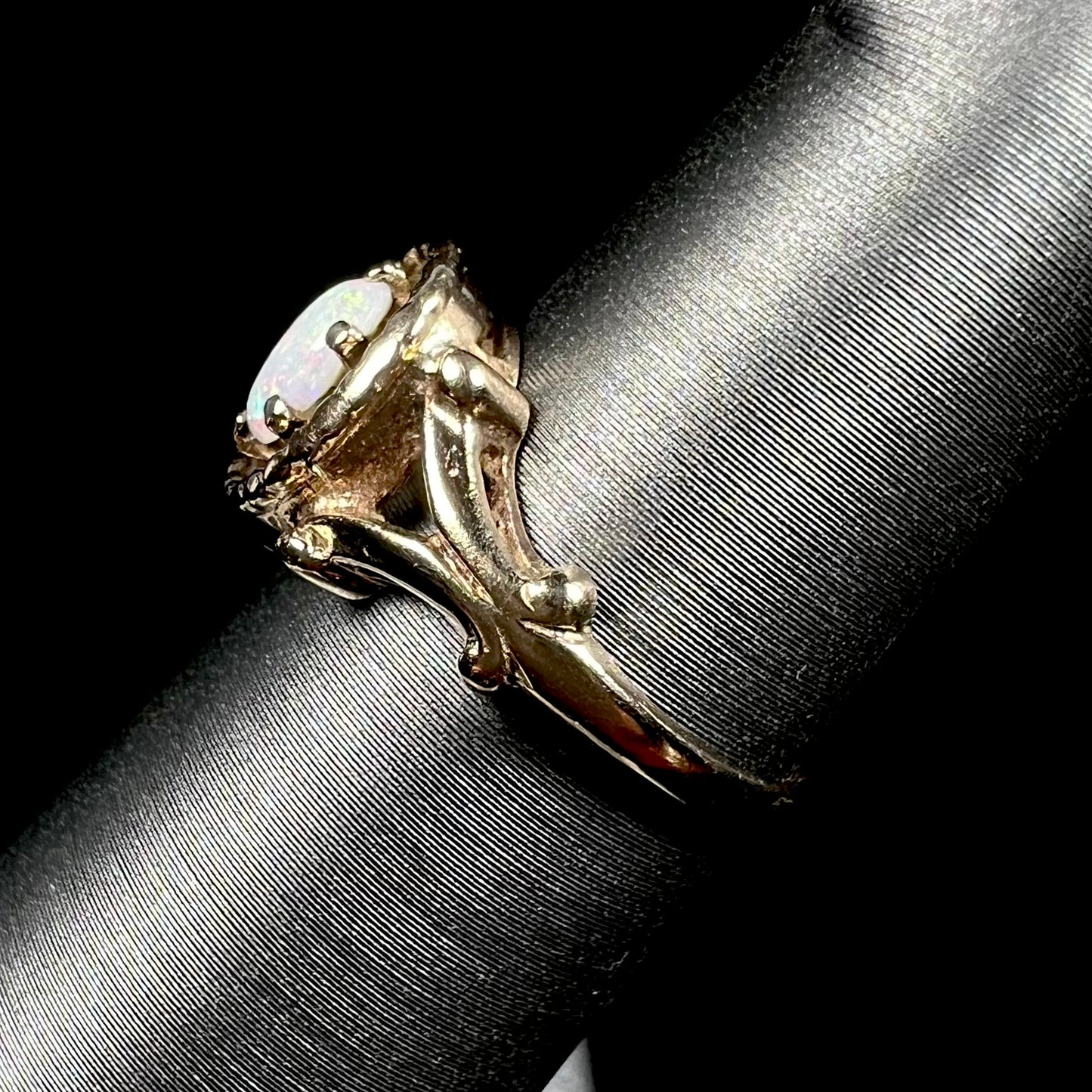 A ladies' Art Nouveau style opal solitaire ring. The mounting is yellow gold with filigree accents.