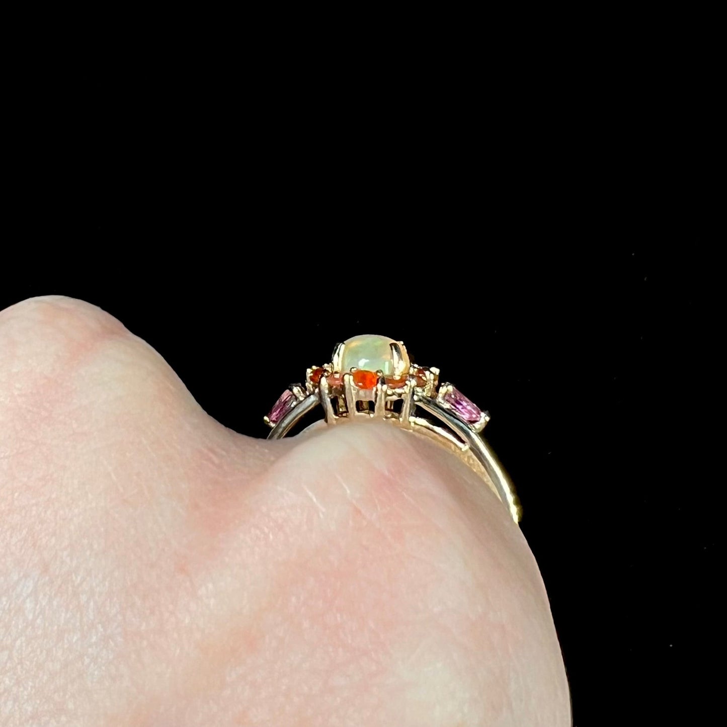 A yellow gold ring mounted with a round Ethiopian opal in a halo of faceted Mexican fire opals. Two pear shaped pink tourmalines accent the sides of the ring.