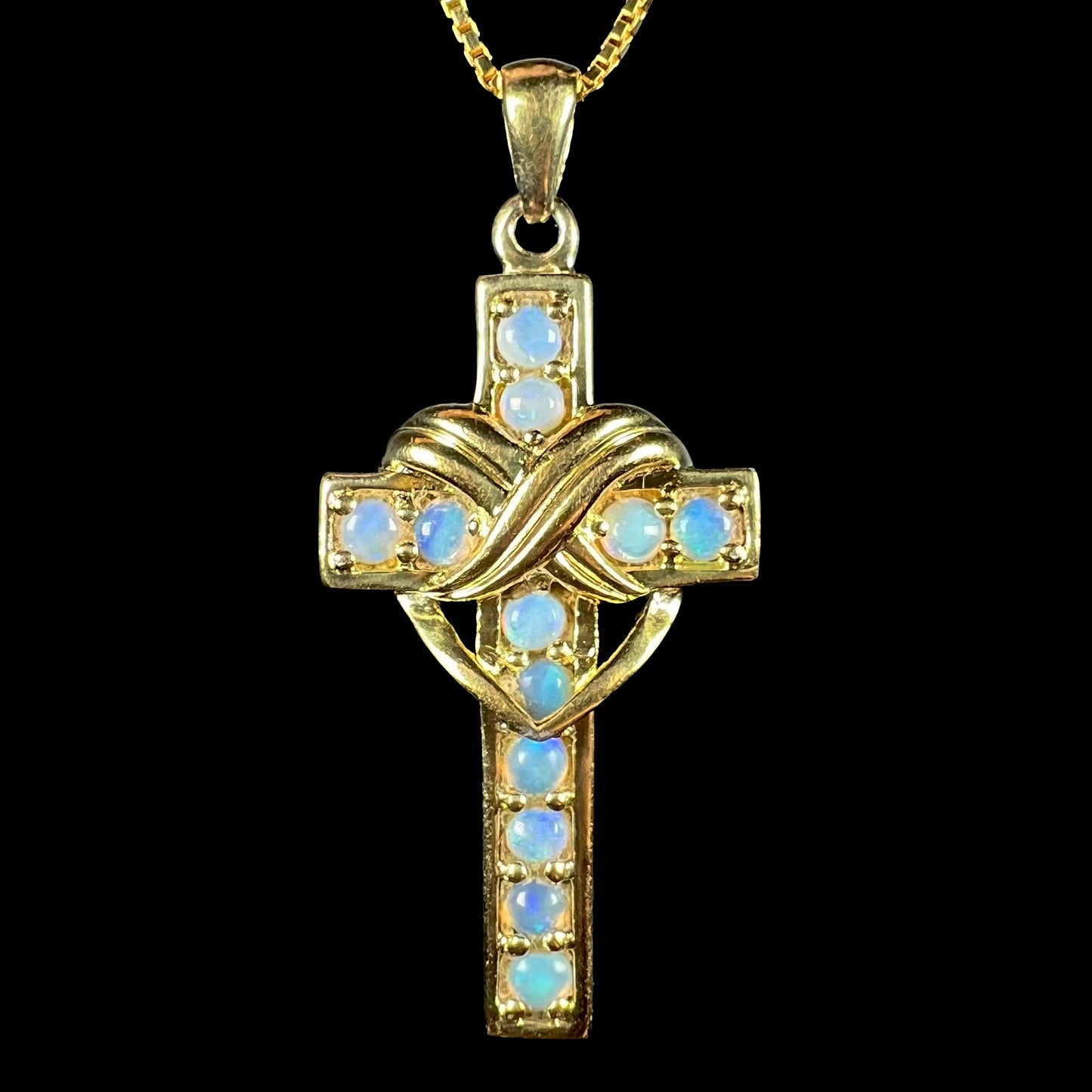 Close-up of gold-tone opal cross necklace against black background.