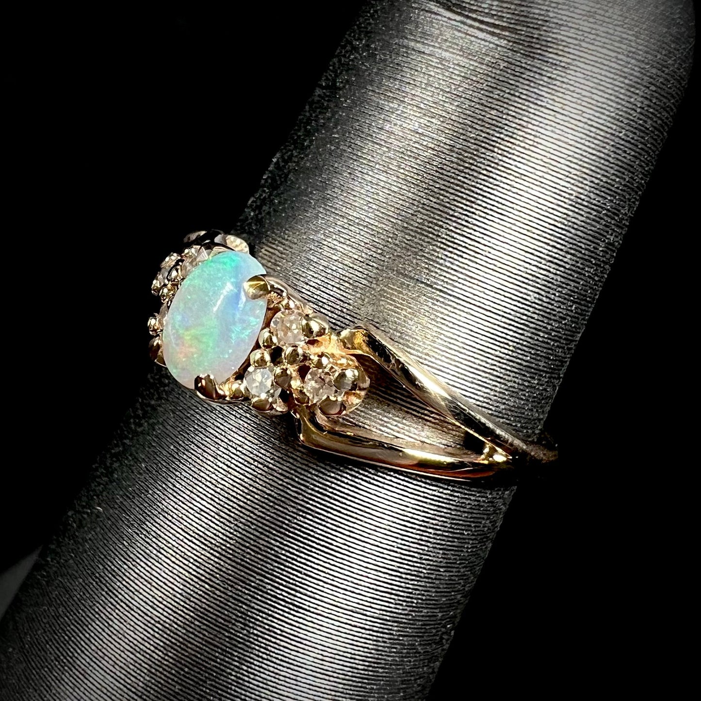 A ladies' yellow gold opal and diamond pinkie ring. The ring is a small size, and the opal shines green and blue colors.