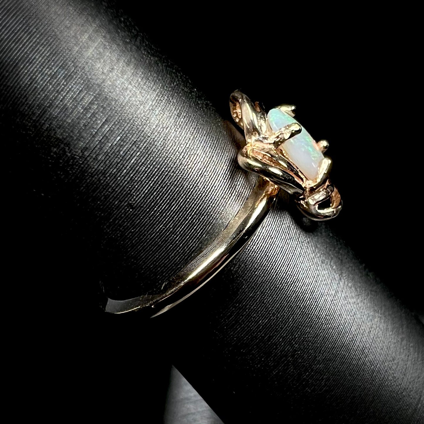 A yellow gold ring mounted with an oval cut opal. The opal has a white base tone with green and blue color play.