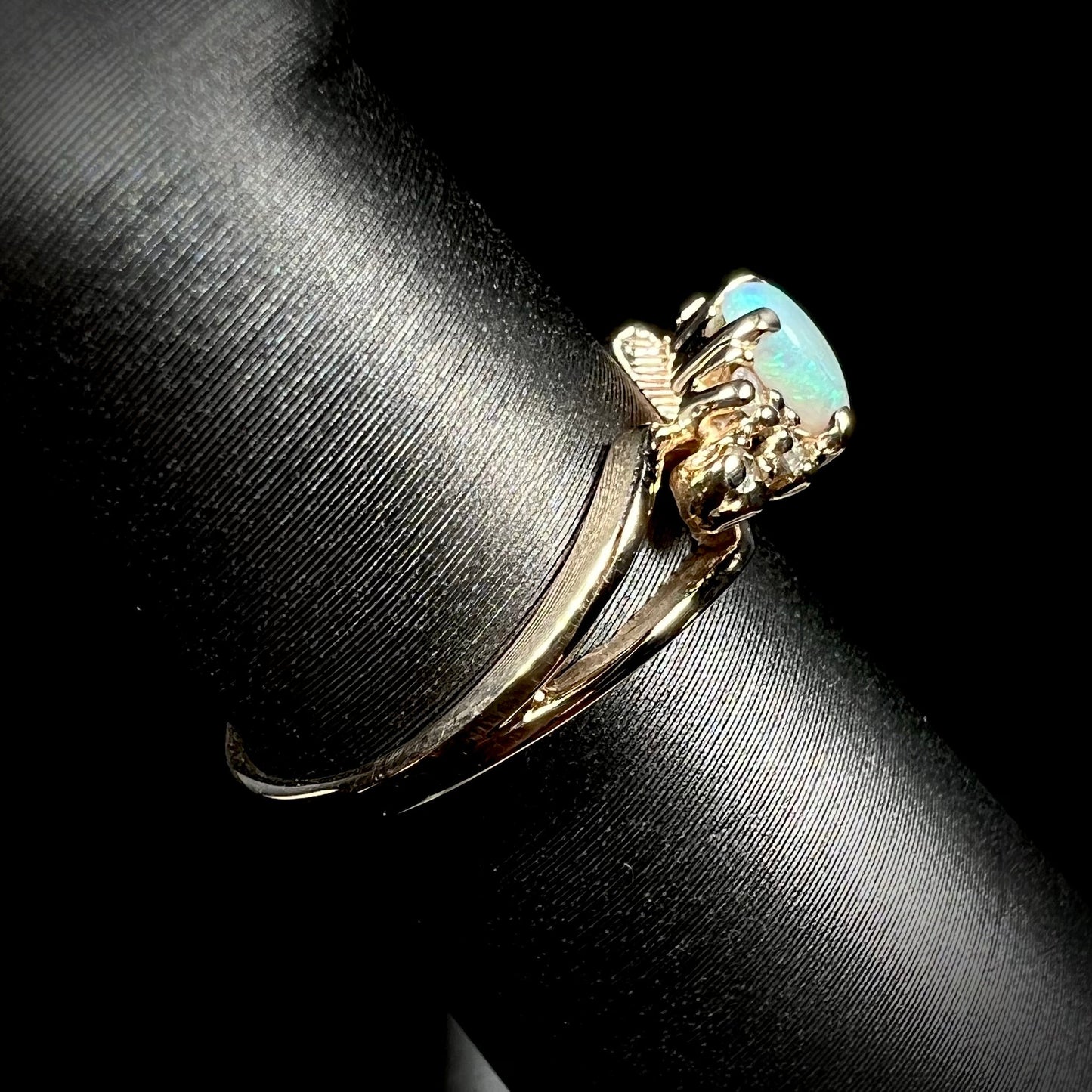 A ladies' yellow gold opal and diamond pinkie ring. The ring is a small size, and the opal shines green and blue colors.