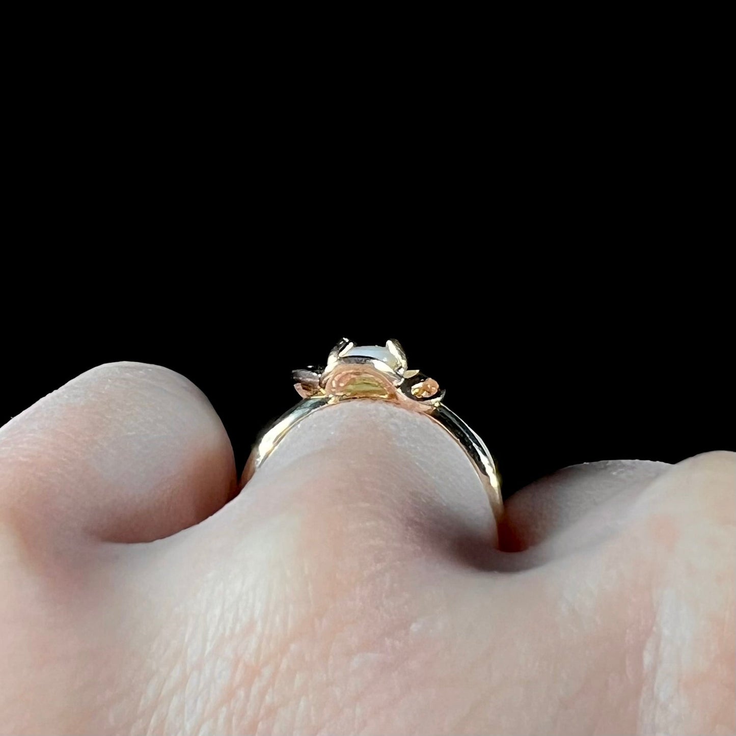 A yellow gold ring mounted with an oval cut opal. The opal has a white base tone with green and blue color play.
