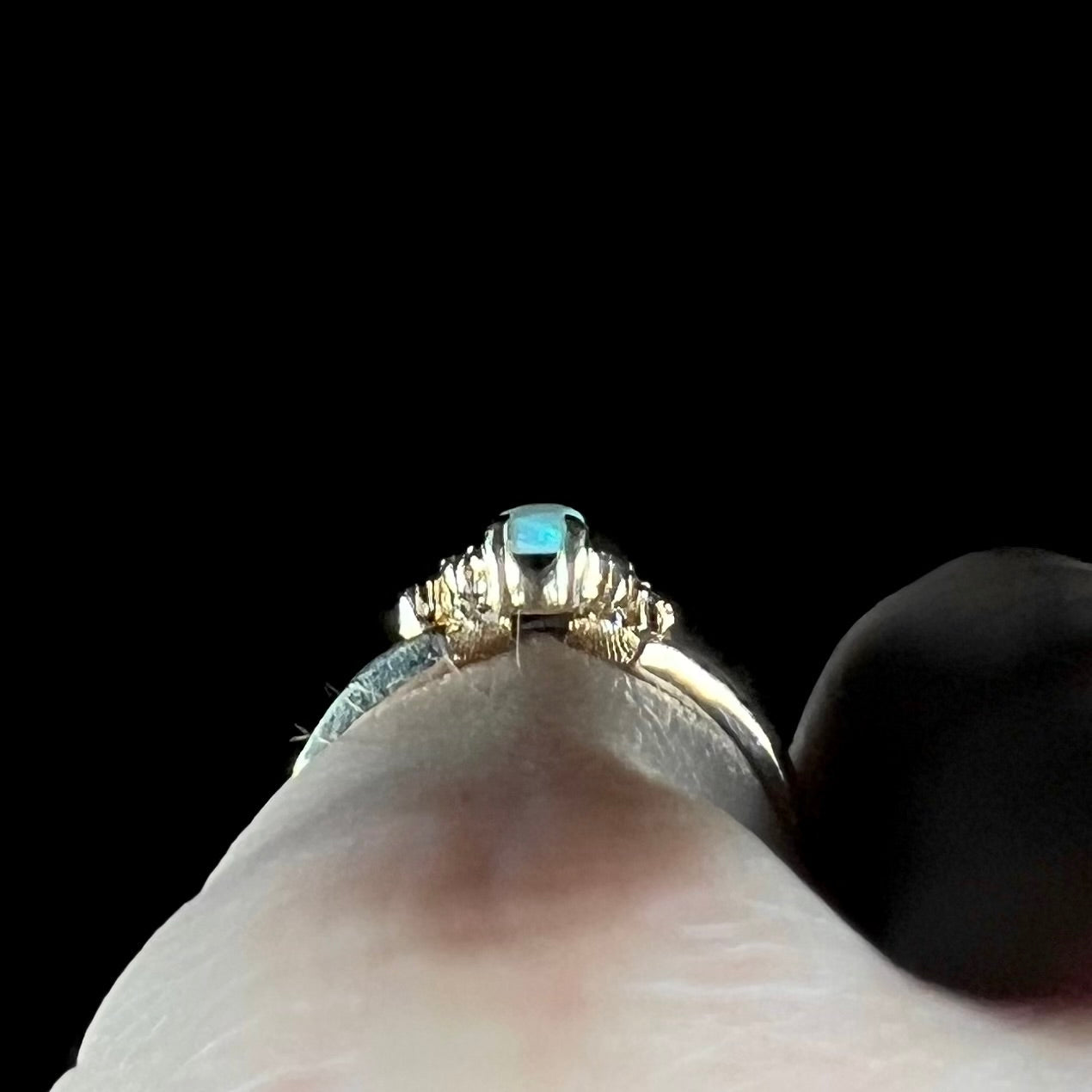 A ladies' yellow gold opal and diamond pinkie ring. The ring is a small size, and the opal shines green and blue colors.