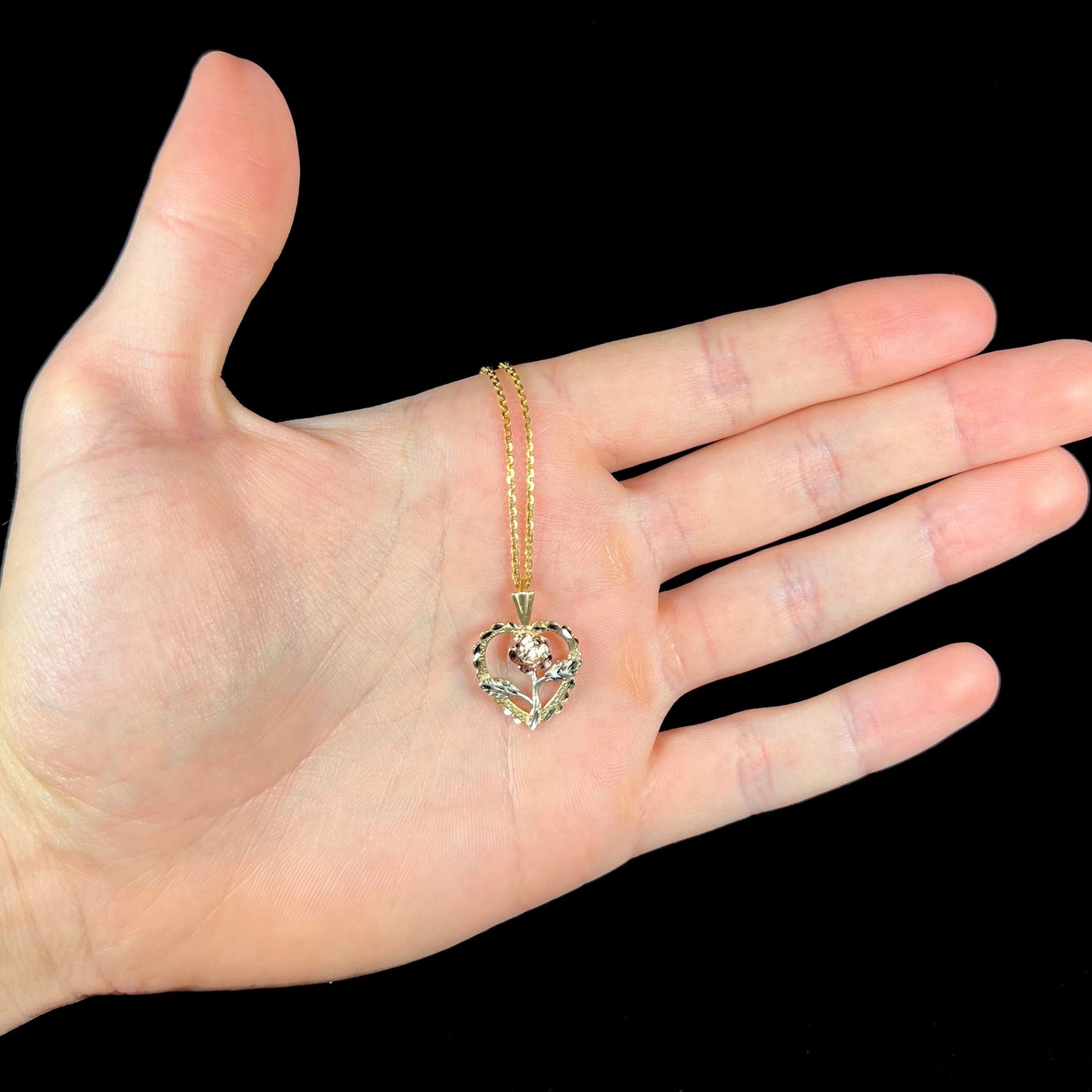 A tricolor gold pendant featuring the design of a heart with a flower in the middle of it.