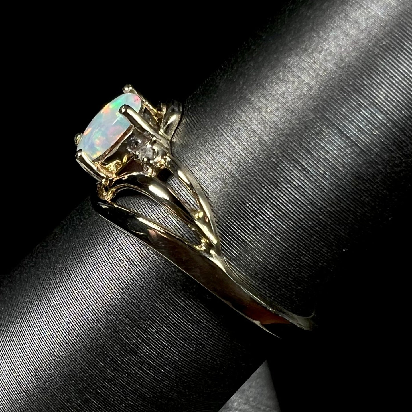 A yellow gold ring mounted with two diamond accents and an oval cut lab created opal. The opal has bright red colors.