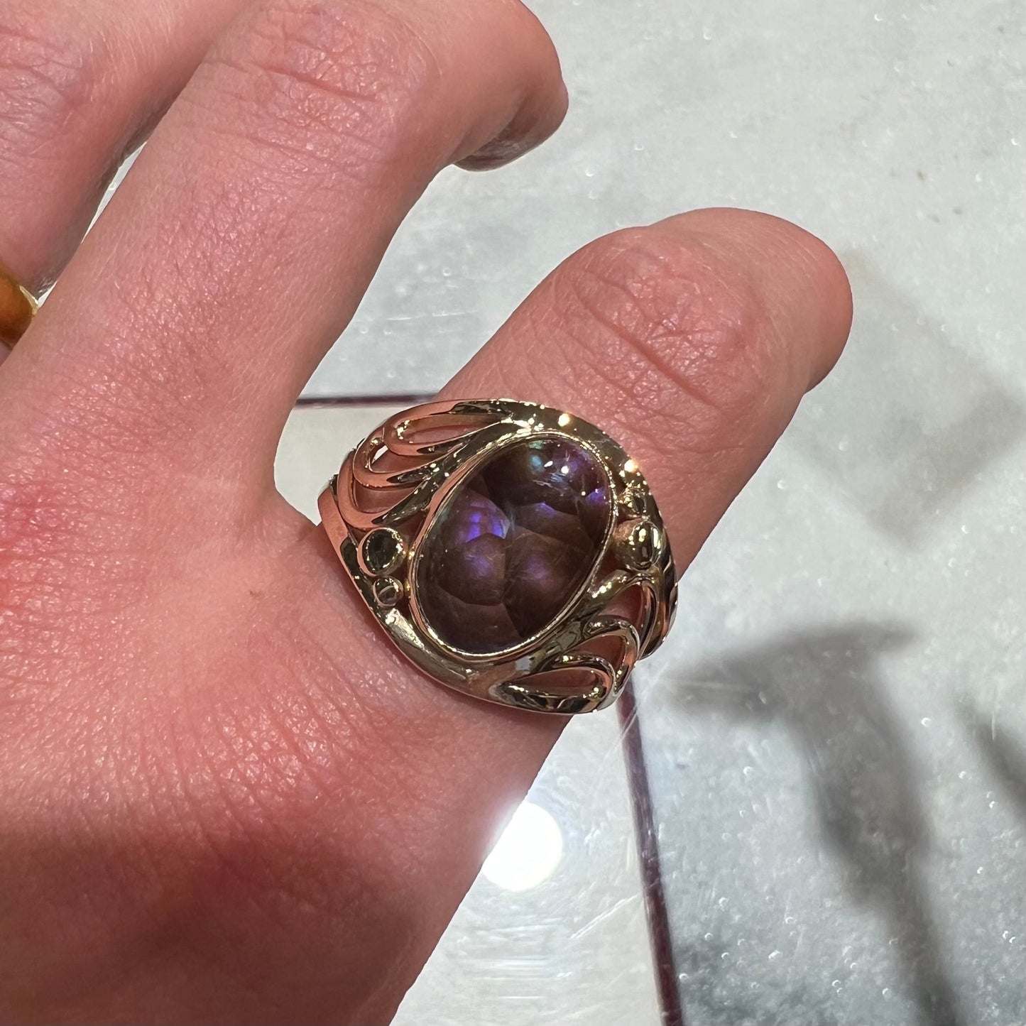 An oval cabochon cut fire agate with purple and blue colors set in a yellow gold men's ring.