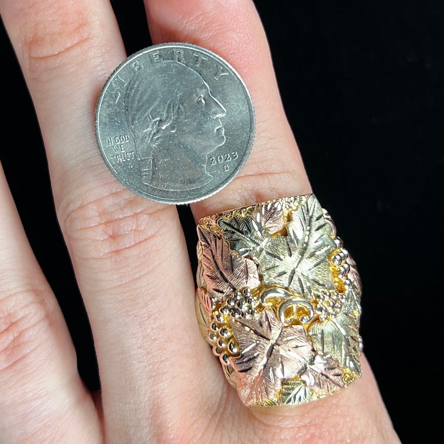 A men's solid gold ring. The ring is Black Hills gold featuring a grapevine and leaf motif with rose and green gold designs.