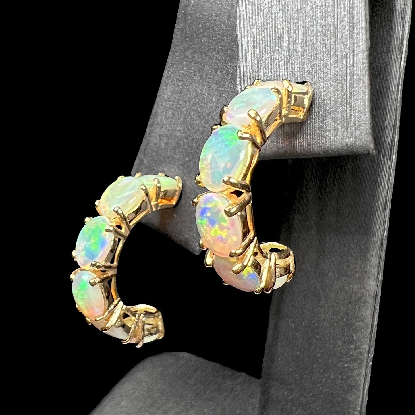A pair of yellow gold opal hoop earrings. Each earring is set with six natural oval cut opals.