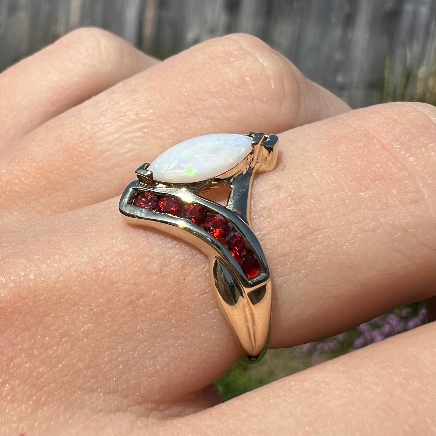 A marquise cut white opal ring. The ring is accented with channel set reddish orange garnets.
