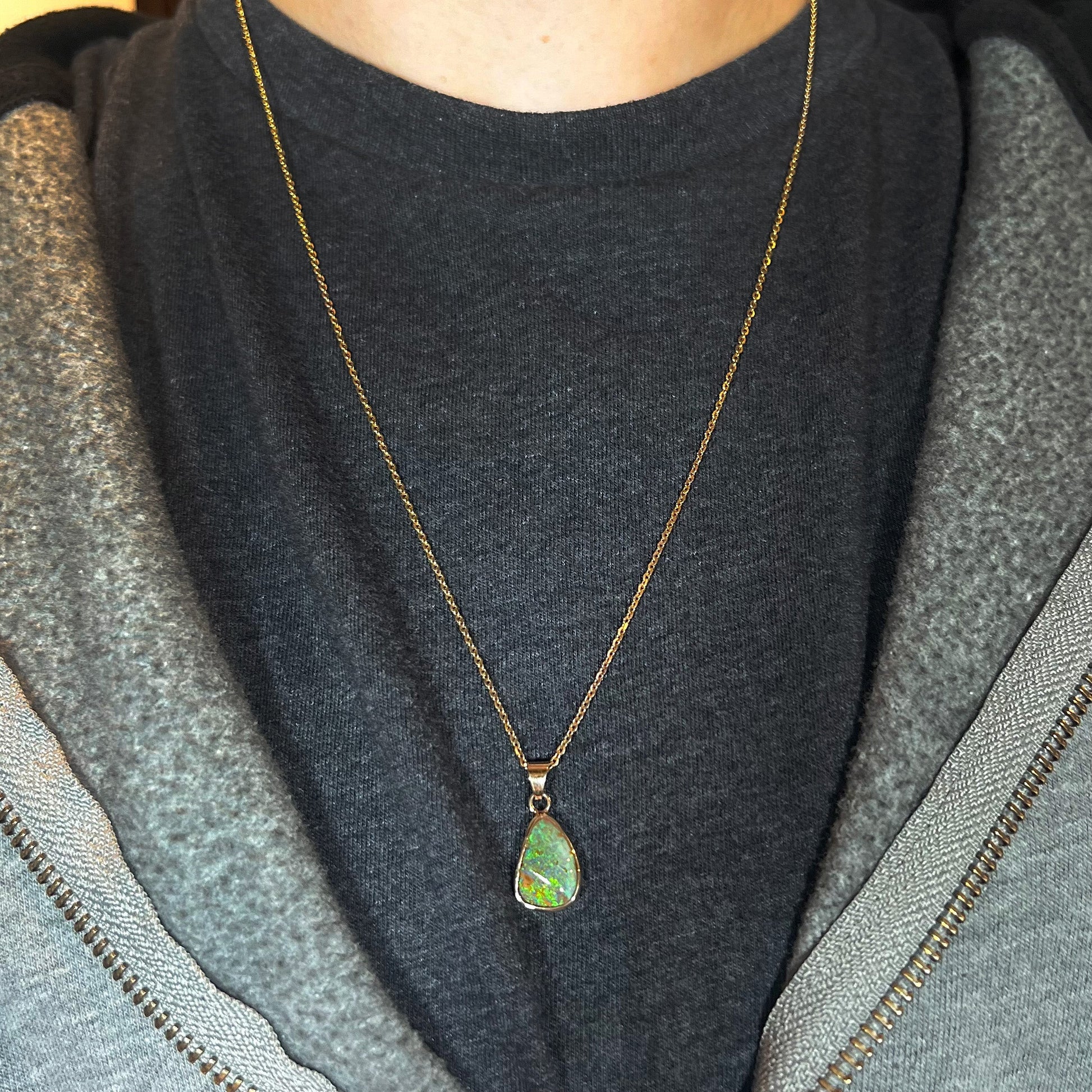 A ladies' natural boulder opal necklace set in 14k yellow gold.  The opal is bezel set and shows green and blue colors.