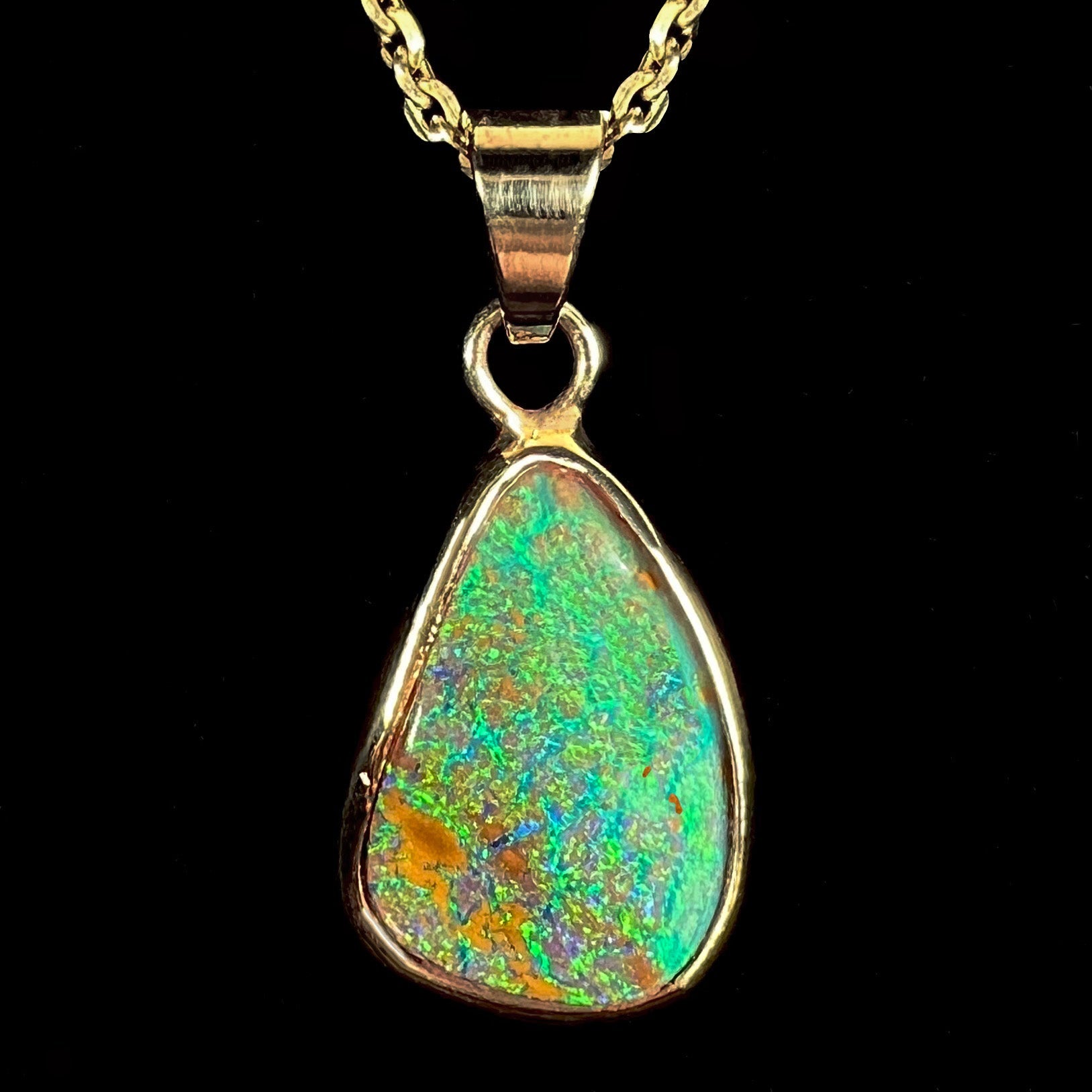 A ladies' natural boulder opal necklace set in 14k yellow gold.  The opal is bezel set and shows green and blue colors.