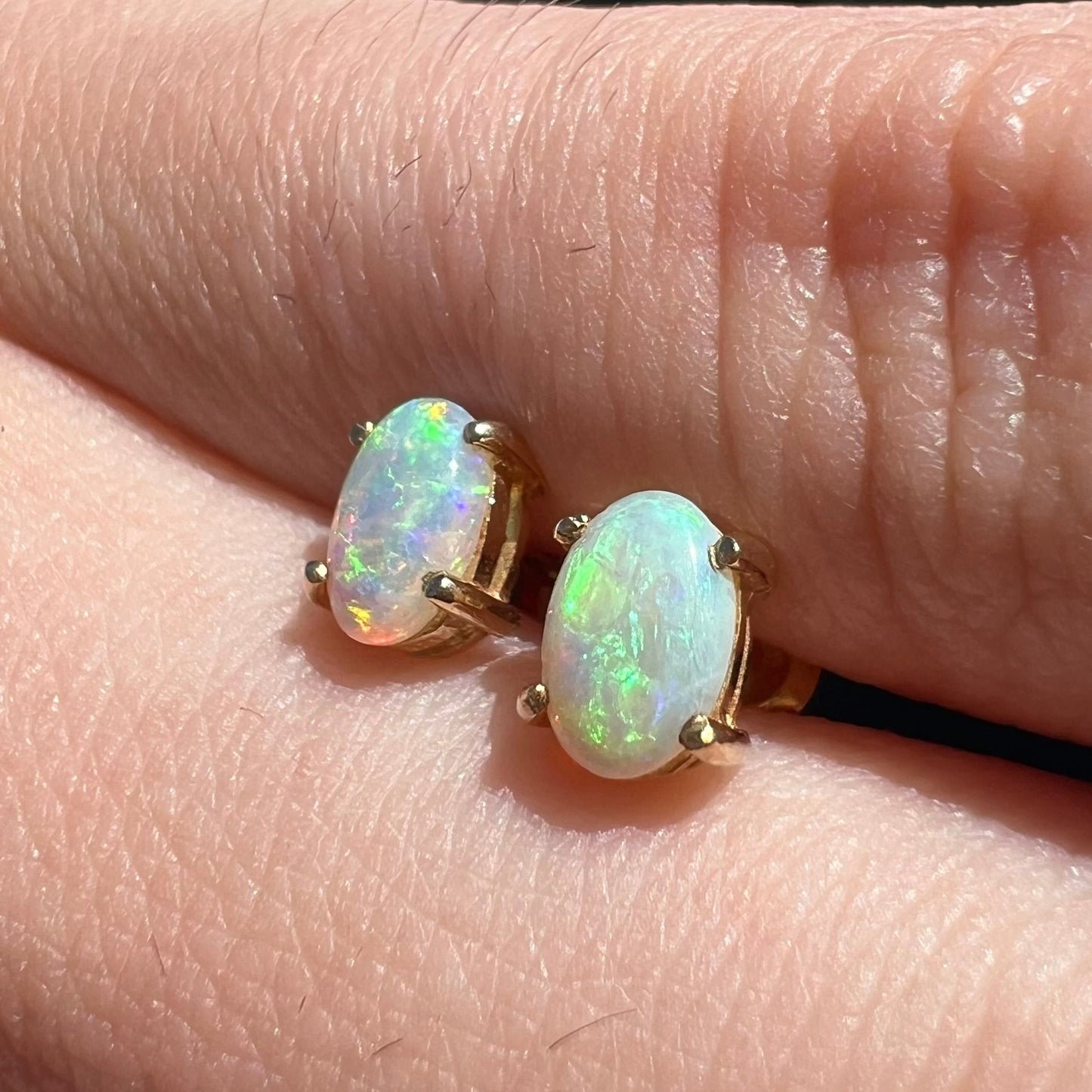 A pair of yellow gold opal stud earrings. The opals have green and blue fire.