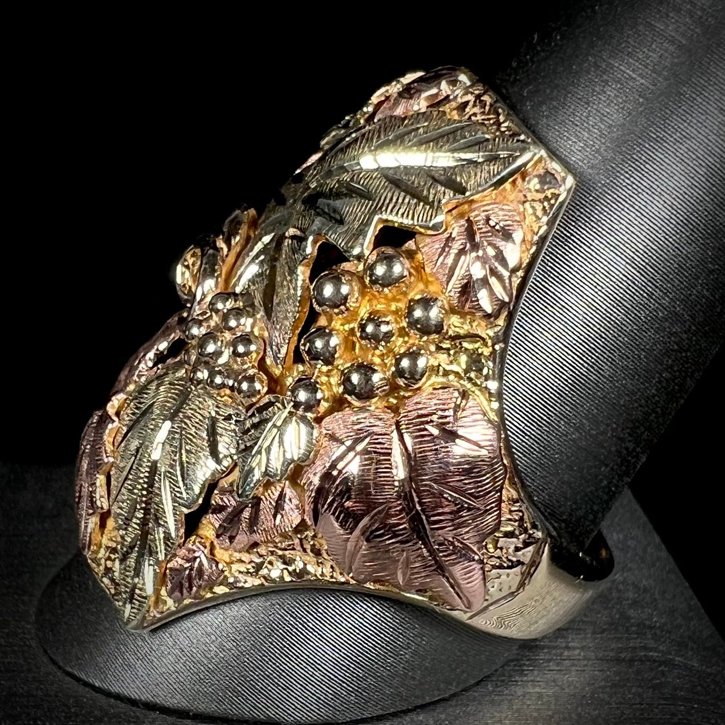 A men's solid gold ring. The ring is Black Hills gold featuring a grapevine and leaf motif with rose and green gold designs.