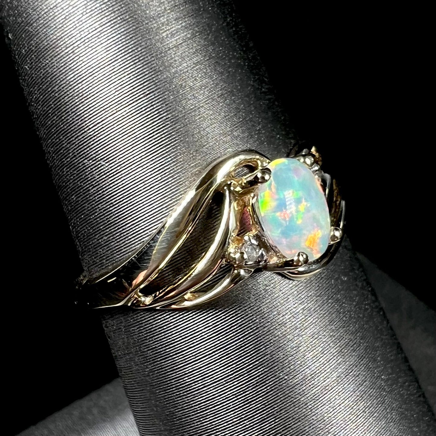 A yellow gold ring mounted with two diamond accents and an oval cut lab created opal. The opal has bright red colors.