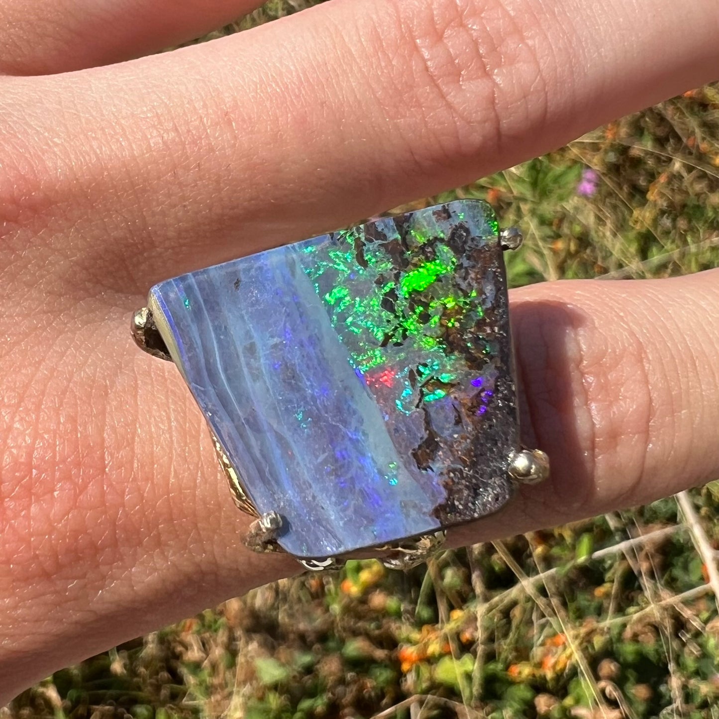 Green flashes play in an Australian boulder opal ring, viewed stright-on, worn on a hand in the sunlight.