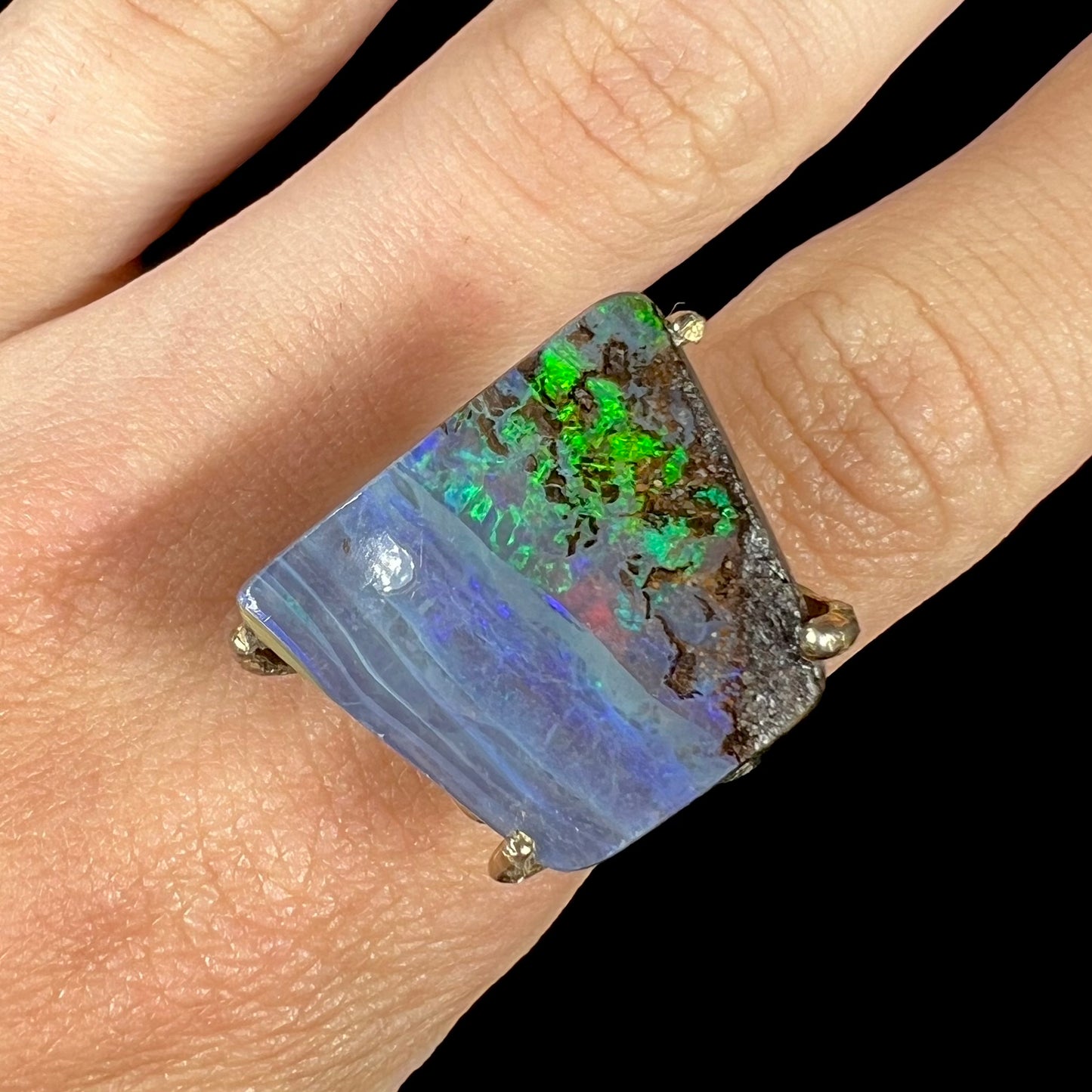 Green flashes seen in a boulder opal ring, worn on a finger against a black background.