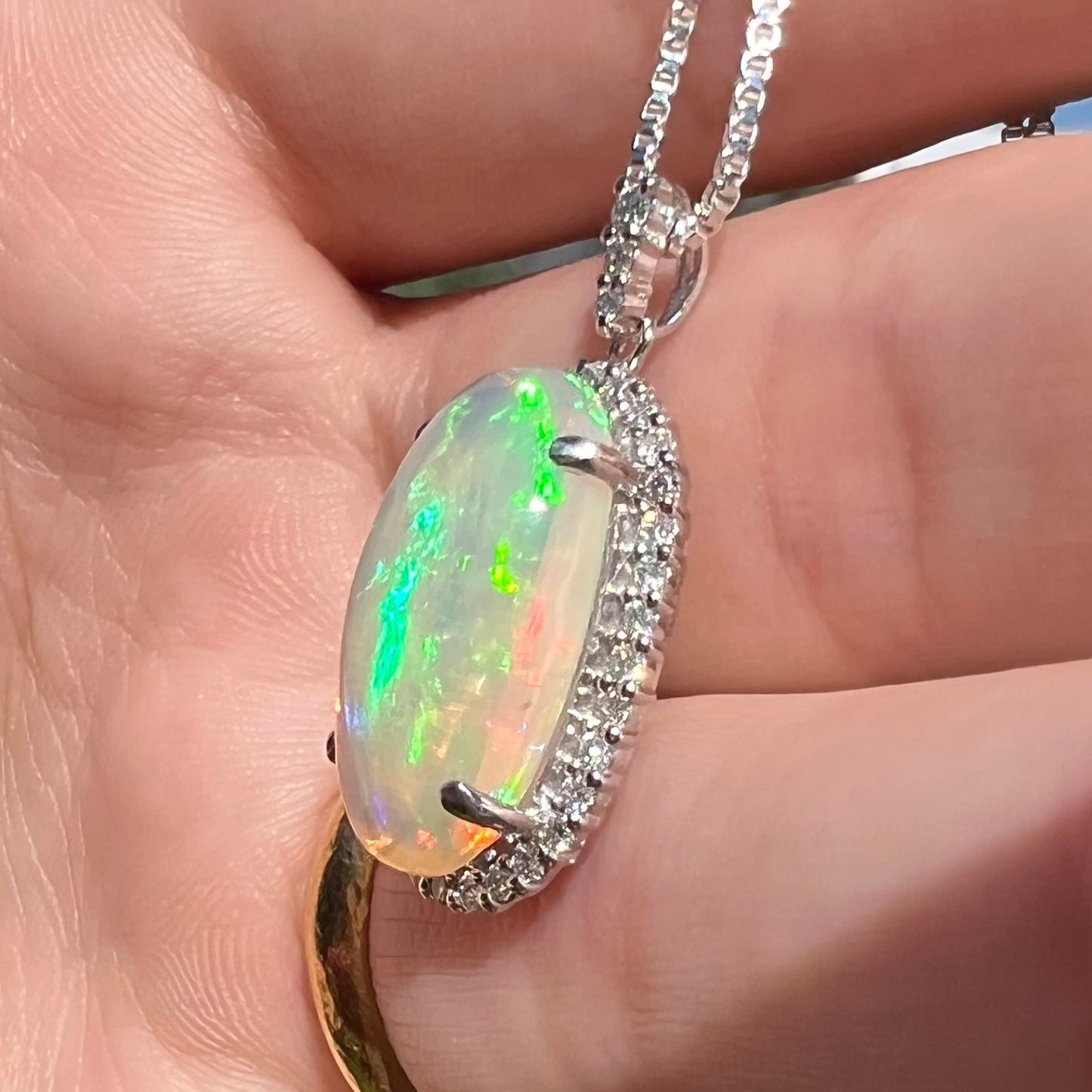 Angled close-up sunlit view of a green Ethiopian opal and diamond platinum pendant held in a hand.