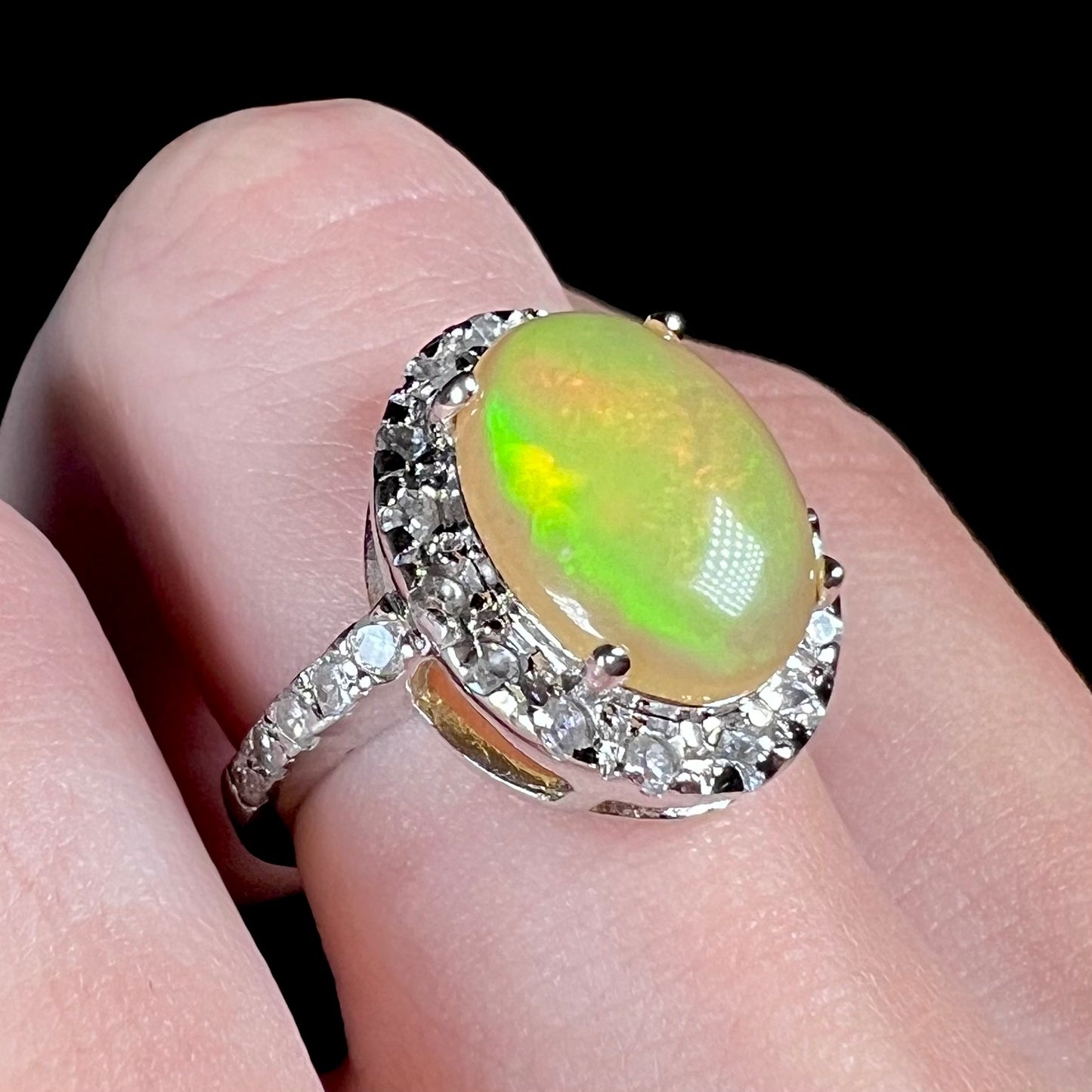 Green color play shines in a sterling silver Ethiopian fire opal ring with a CZ halo, pictured on a hand at an angled view.