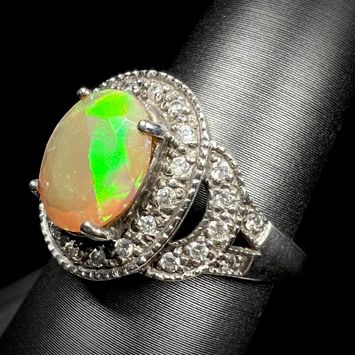 Angled view of green Ethiopian opal ring with cubic zirconia halo against black background.