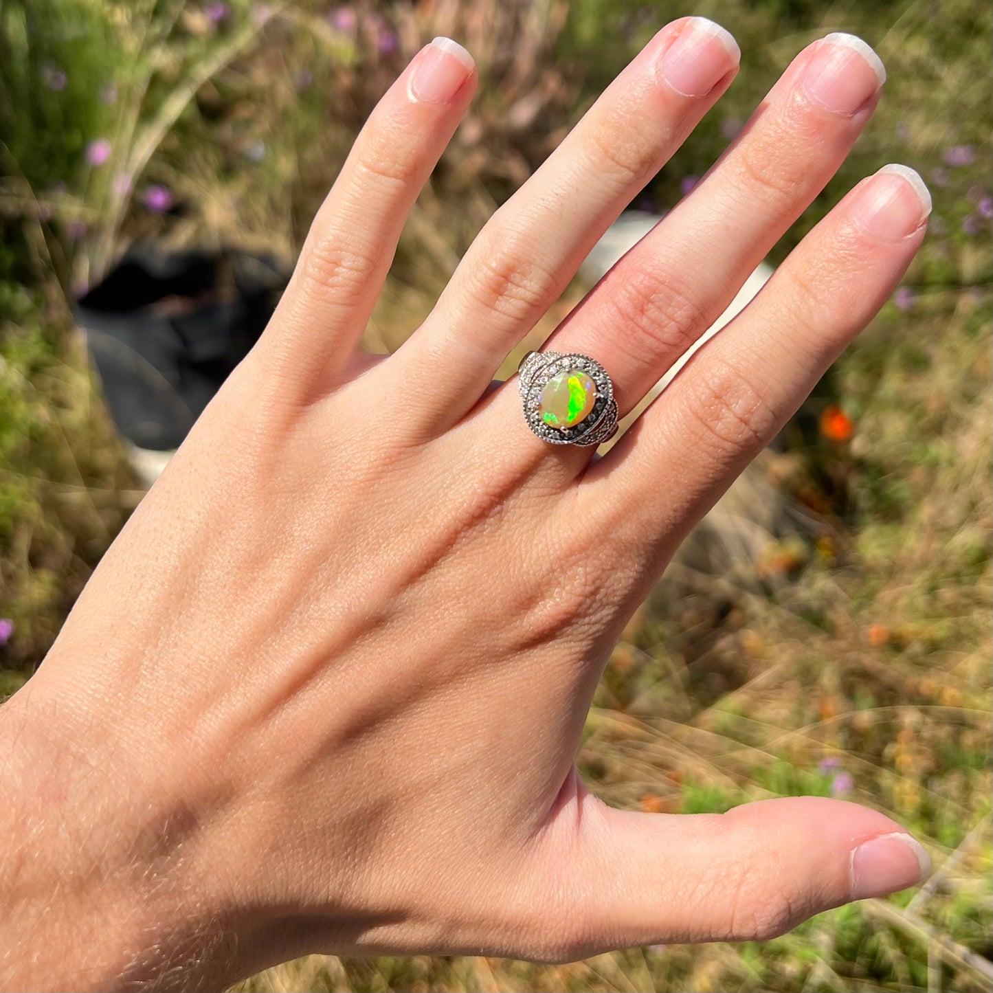 A green Ethiopian opal ring with a cubic zirconia halo, worn on a hand in natural daylight.