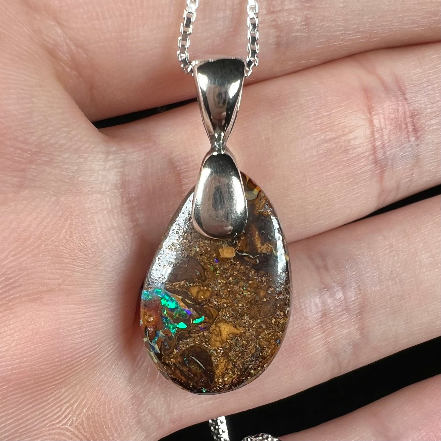 An Australian boulder opal necklace with a sterling silver bail. The opal has a bright green flash of color.