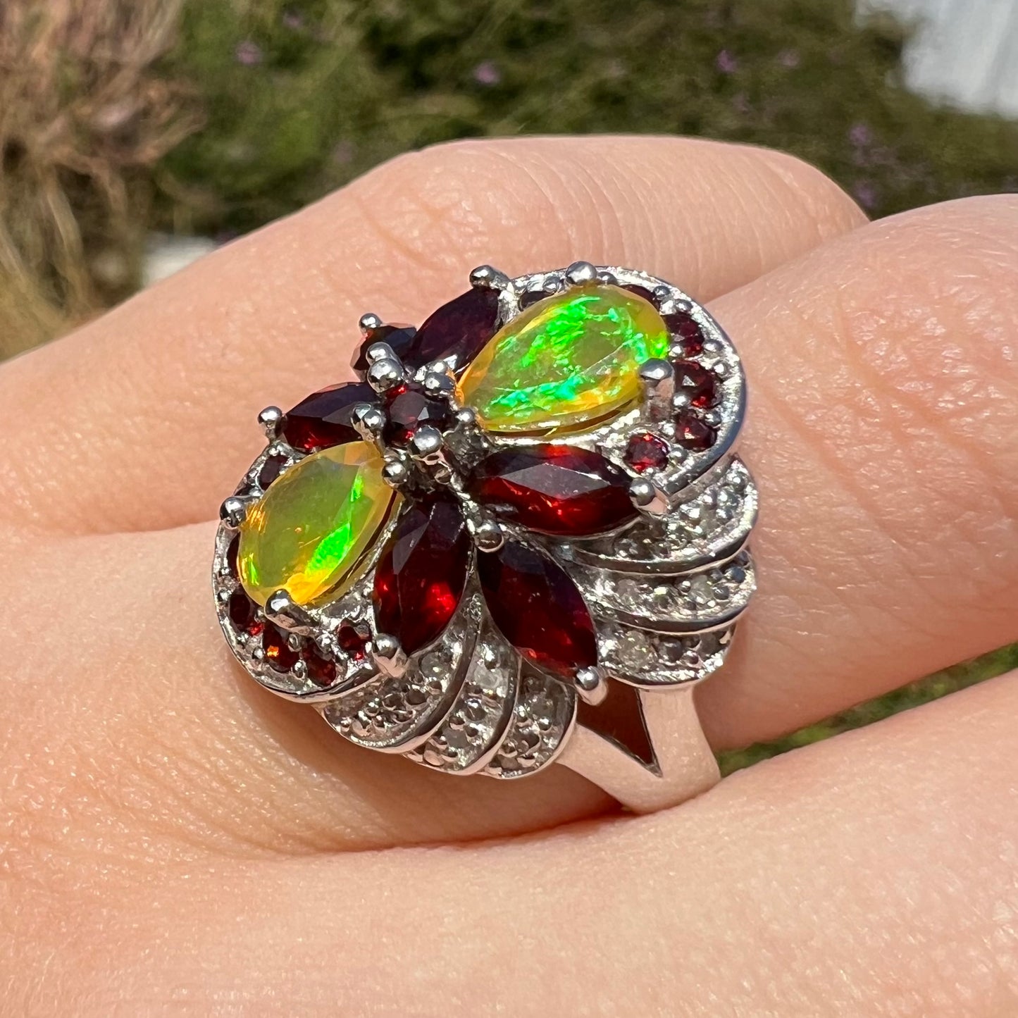 A sterling silver Ethiopian opal and garnet infinity-design ring, shown at an angle in sunlight. The opals are green.