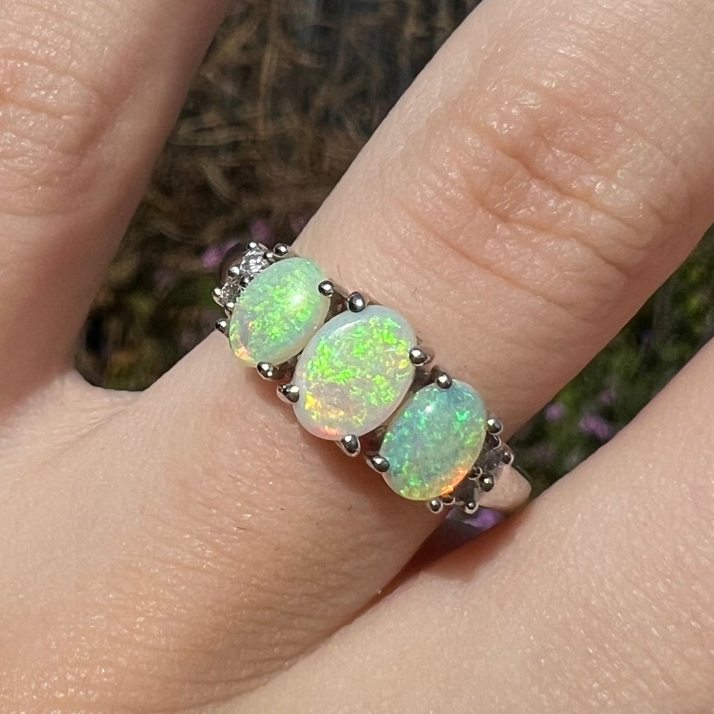 A ladies' white gold ring prong-set with three natural white opals and diamond accents. The opals play a green color.
