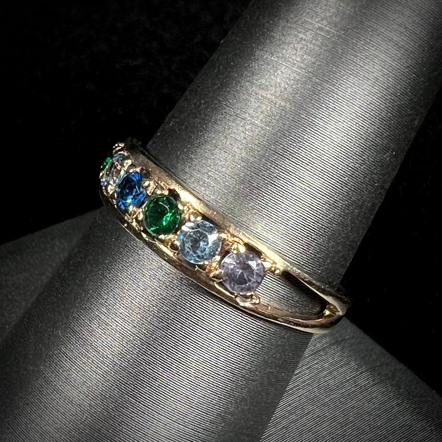 A ladies' yellow gold band set with green, dark blue, light blue, and light purple stones.