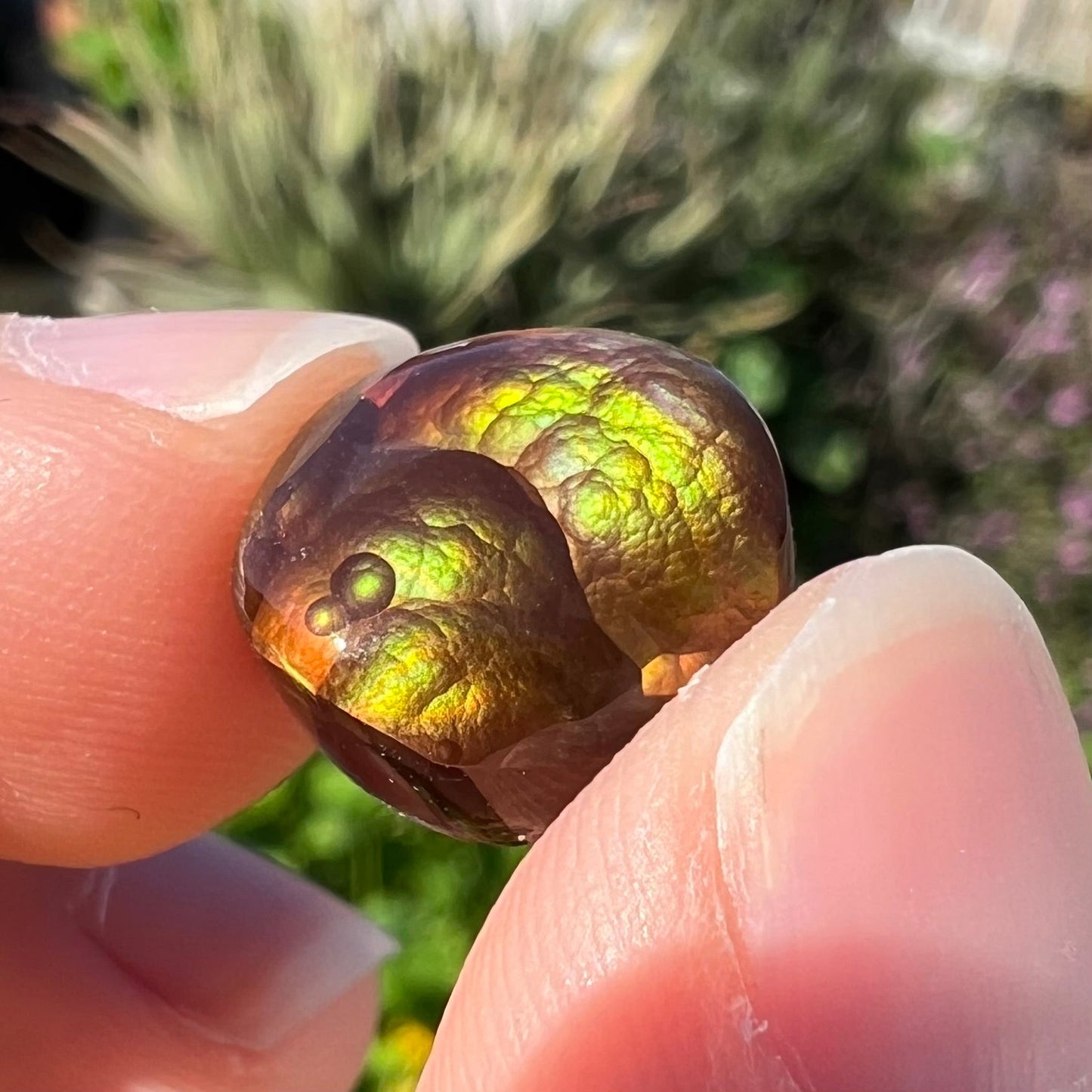 A loose, round Mexican fire agate stone. The stone shines colors of green, yellow, and orange.