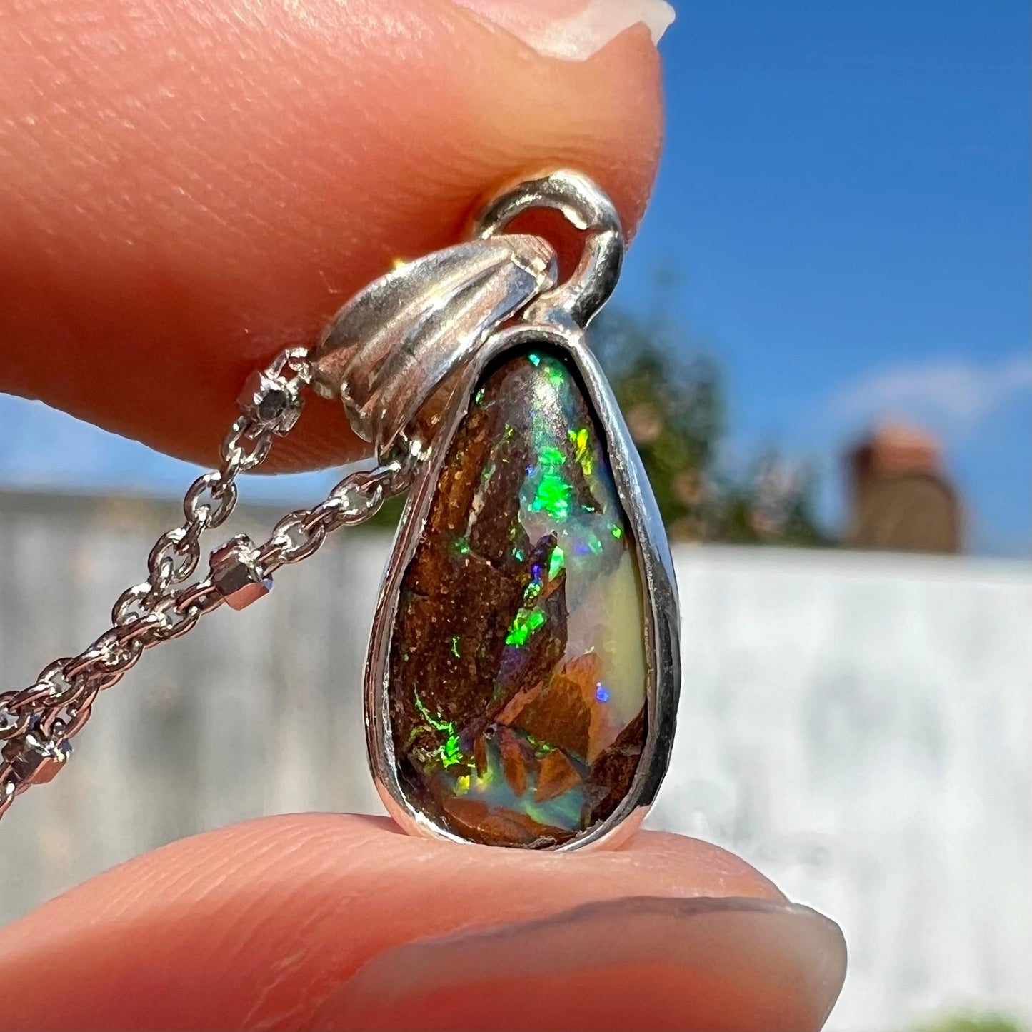 A pear shaped boulder opal necklace in sterling silver. The opal has bright green and blue flashes.