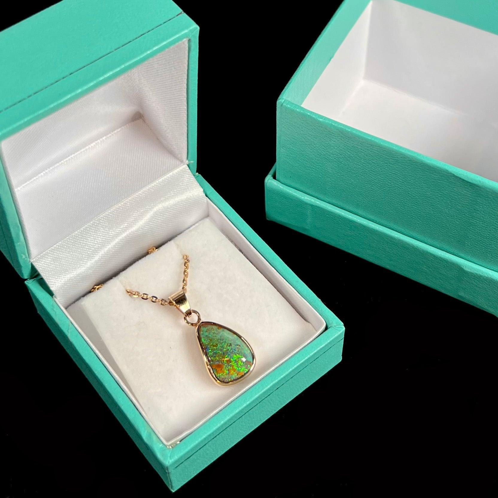A ladies' natural boulder opal necklace set in 14k yellow gold.  The opal is bezel set and shows green and blue colors.