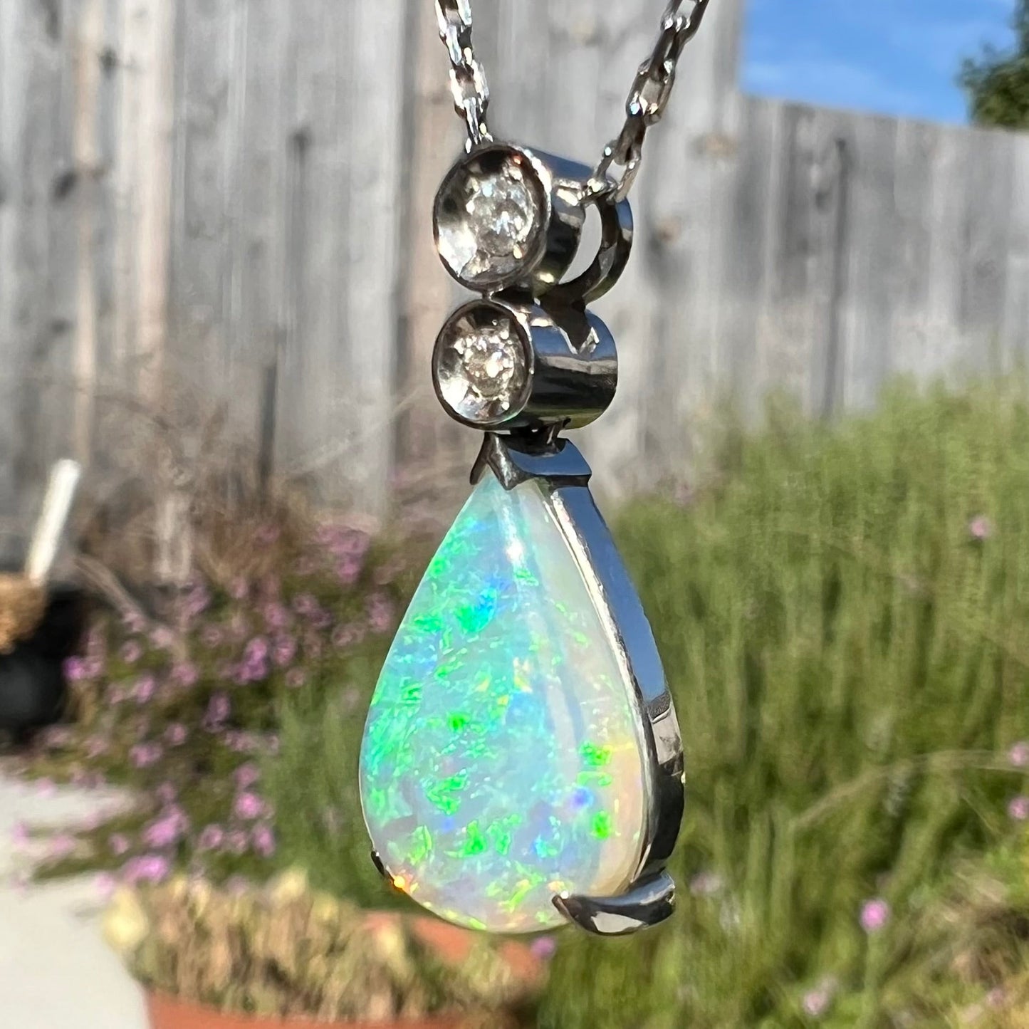 A platinum drop pendant mounted with two diamond accents and a pear shaped green-blue crystal opal.