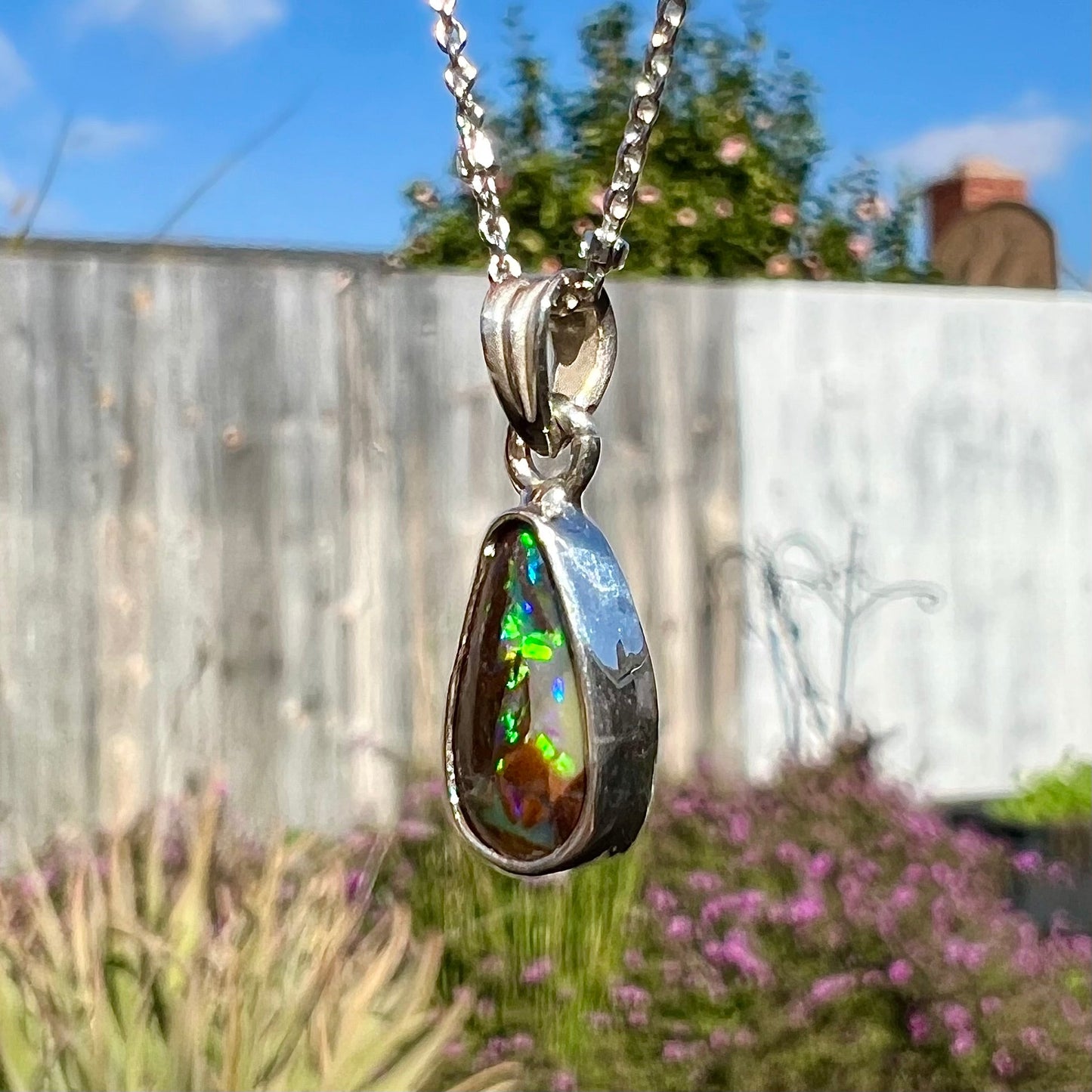 A pear shaped boulder opal necklace in sterling silver. The opal has bright green and blue flashes.