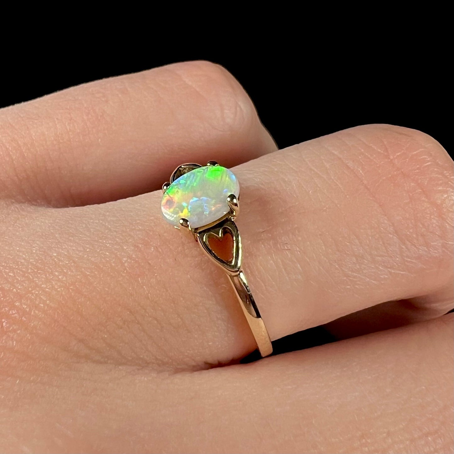 A dainty yellow gold ring mounted with a vivdly bright red Australian opal. The ring has two heart shaped designs.