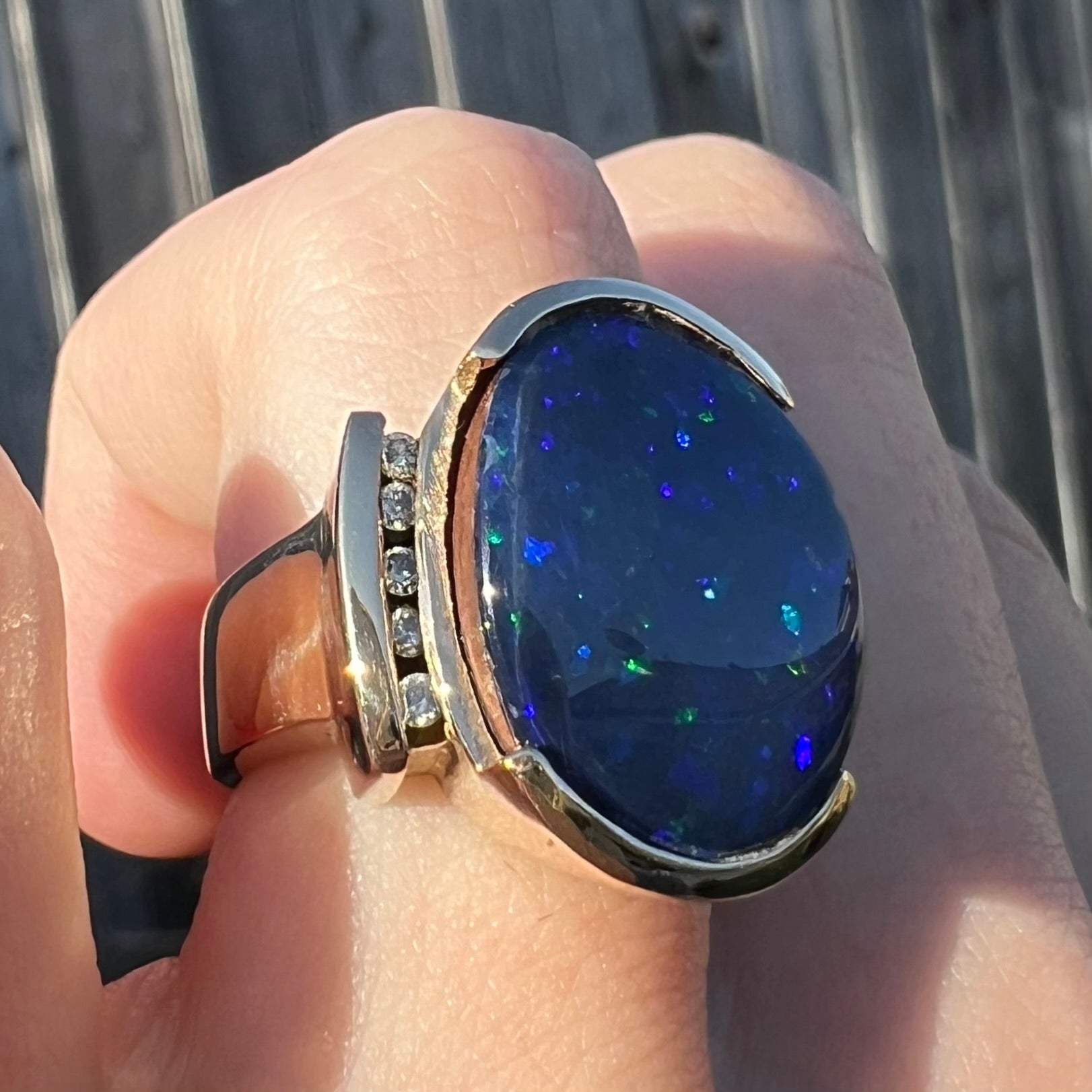 A large, unisex gold ring mounted with a half-bezel set black opal doublet and diamonds.