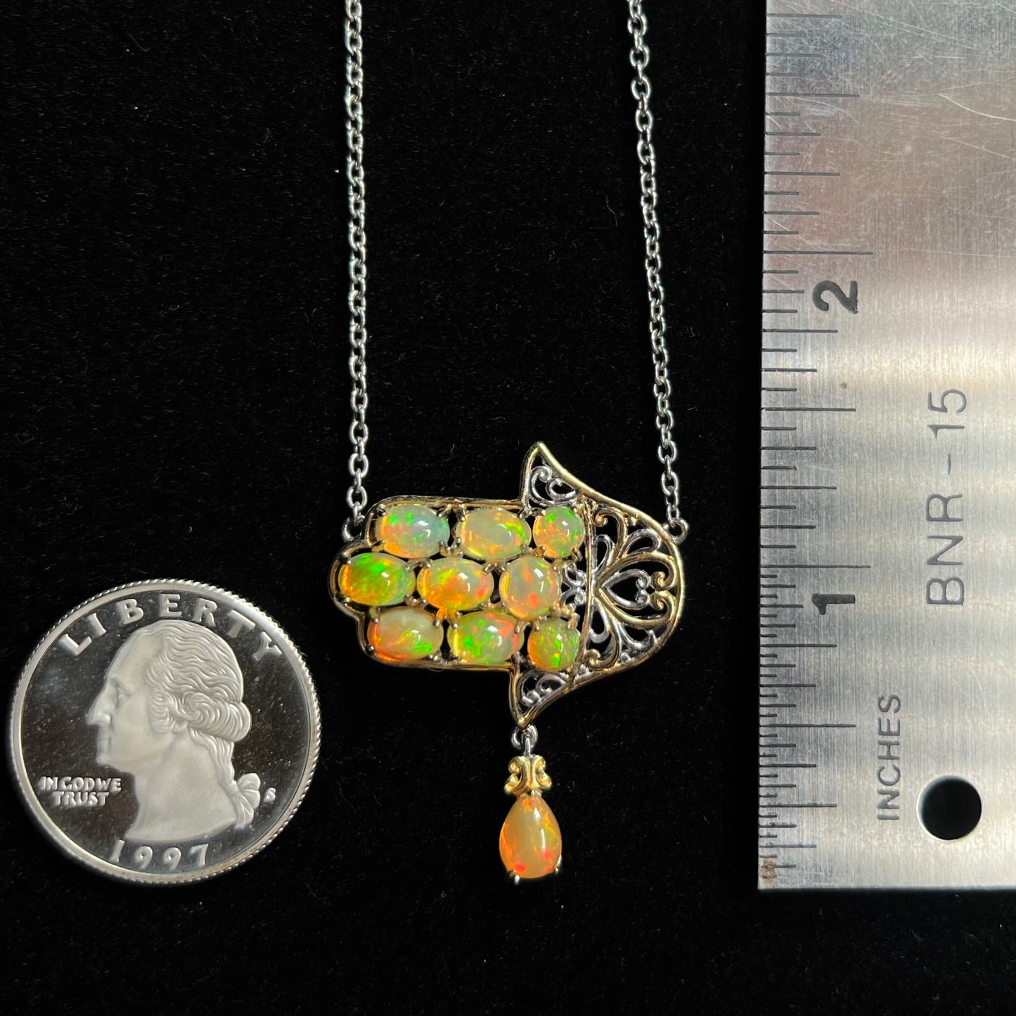 A hamsa opal necklace rested next to a quarter coin and ruler for scale.