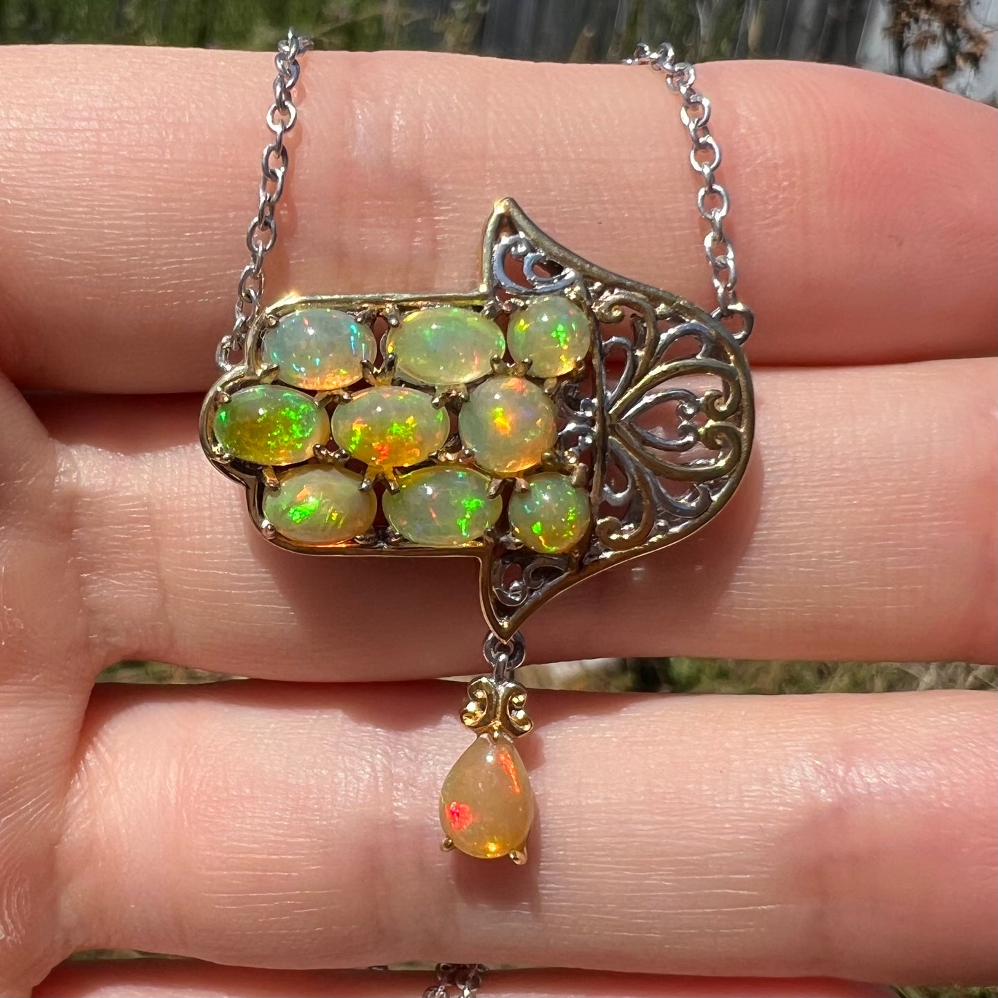 A hamsa opal necklace shown from the front, close-up, in a hand in the sunlight.