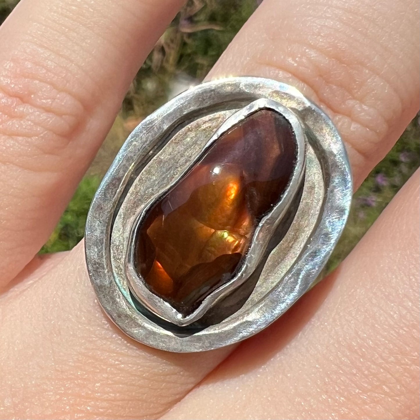 Close-up of a handmade sterling silver fire agate ring, worn on a finger in the sunlight.