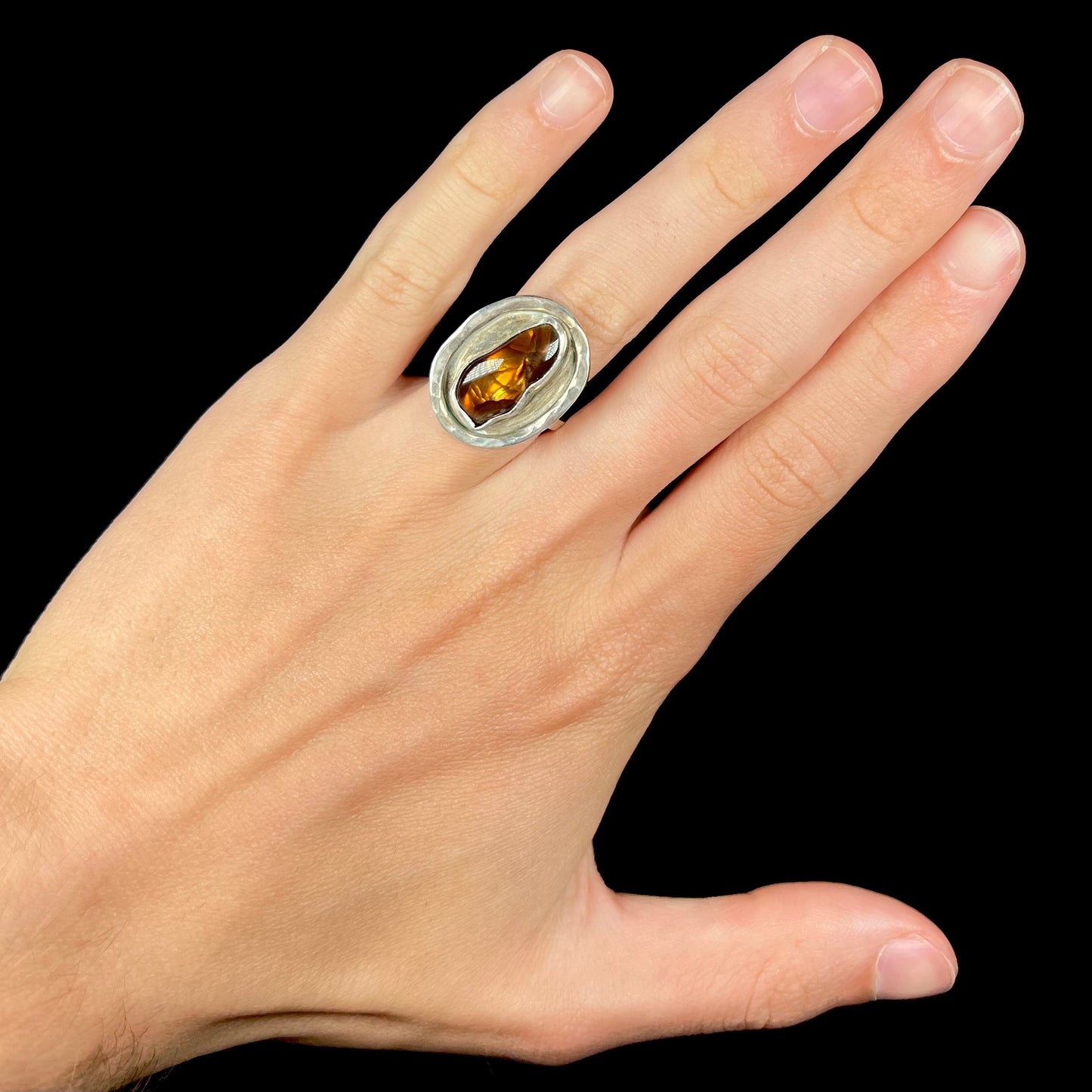 A handmade sterling silver fire agate ring worn on a hand against a black background.