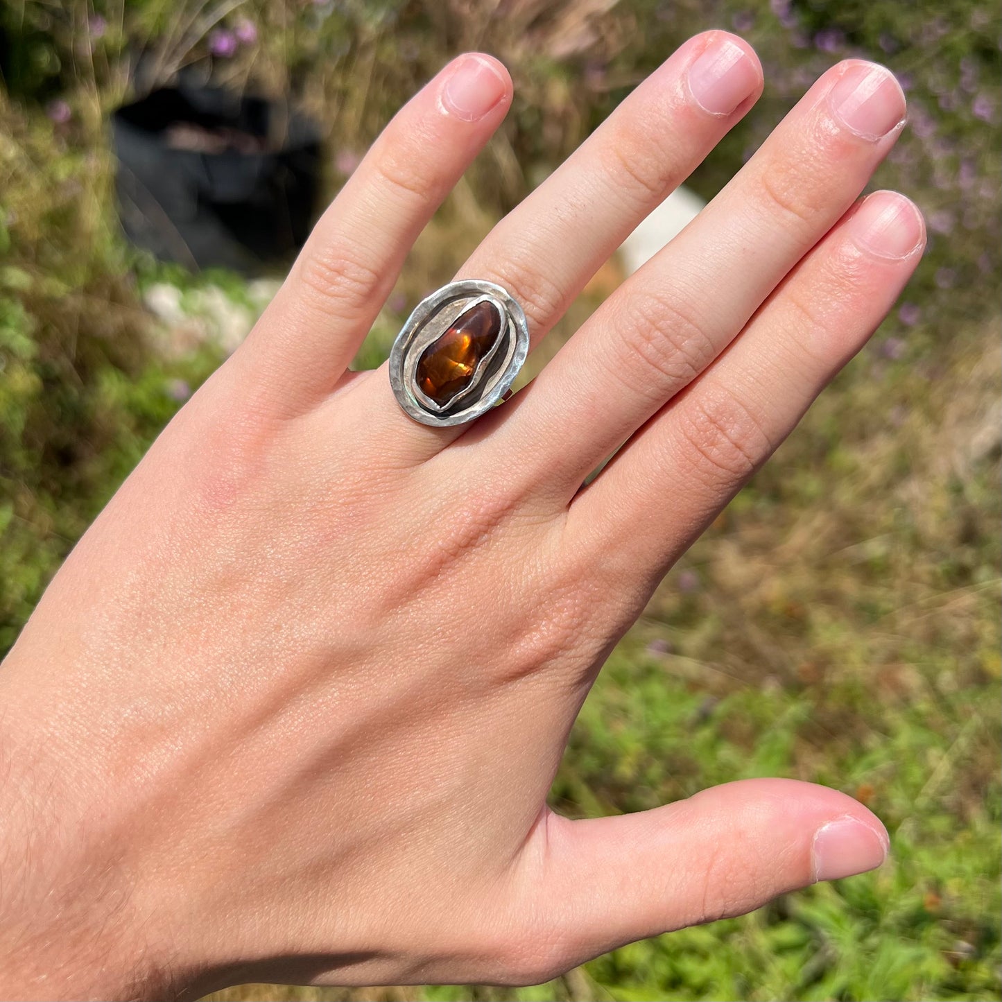 A handmade sterling silver fire agate ring worn on a hand in the sunlight against an outdoor background.