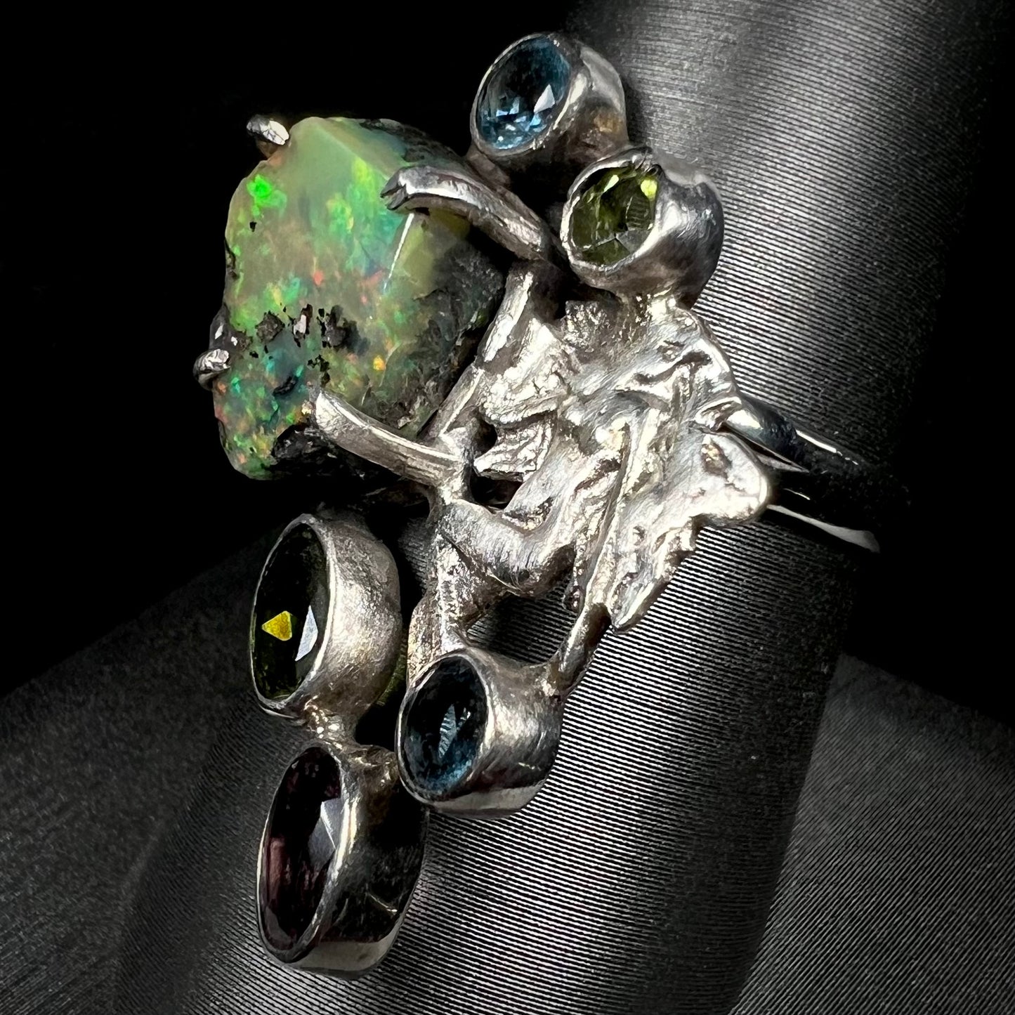 Angled view of a silver men's ring set with rough Virgin Valley opal and gems with a female figure design.