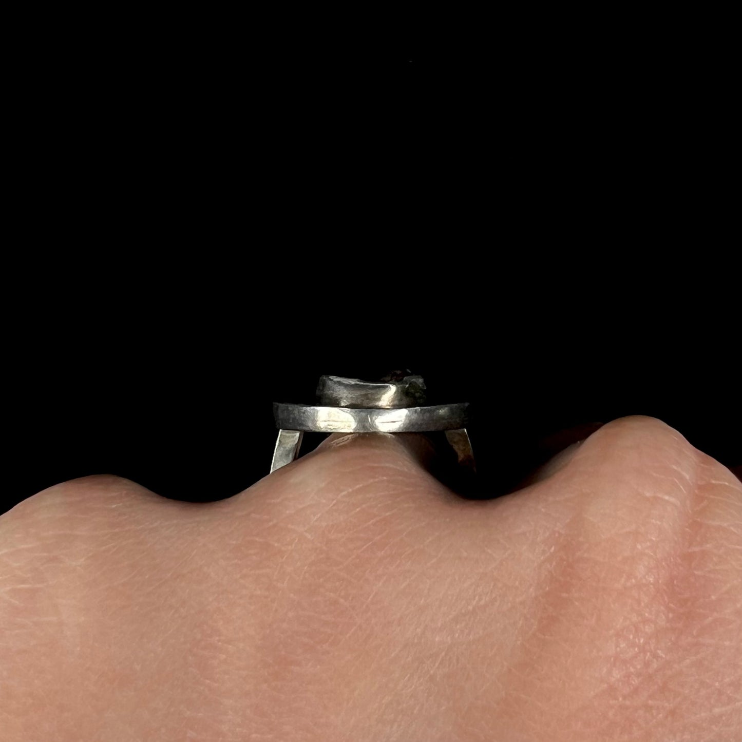 Side profile view of a handmade sterling silver fire agate ring worn on a hand.