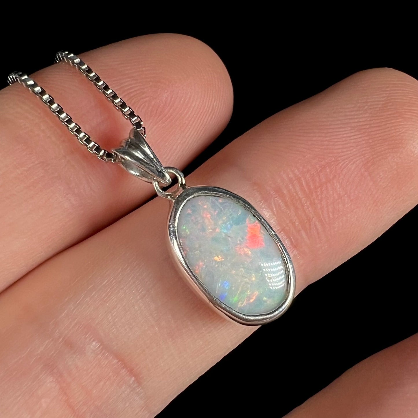 A ladies' sterling silver necklace bezel set with a natural white crystal opal. The opal has red and blue fire.