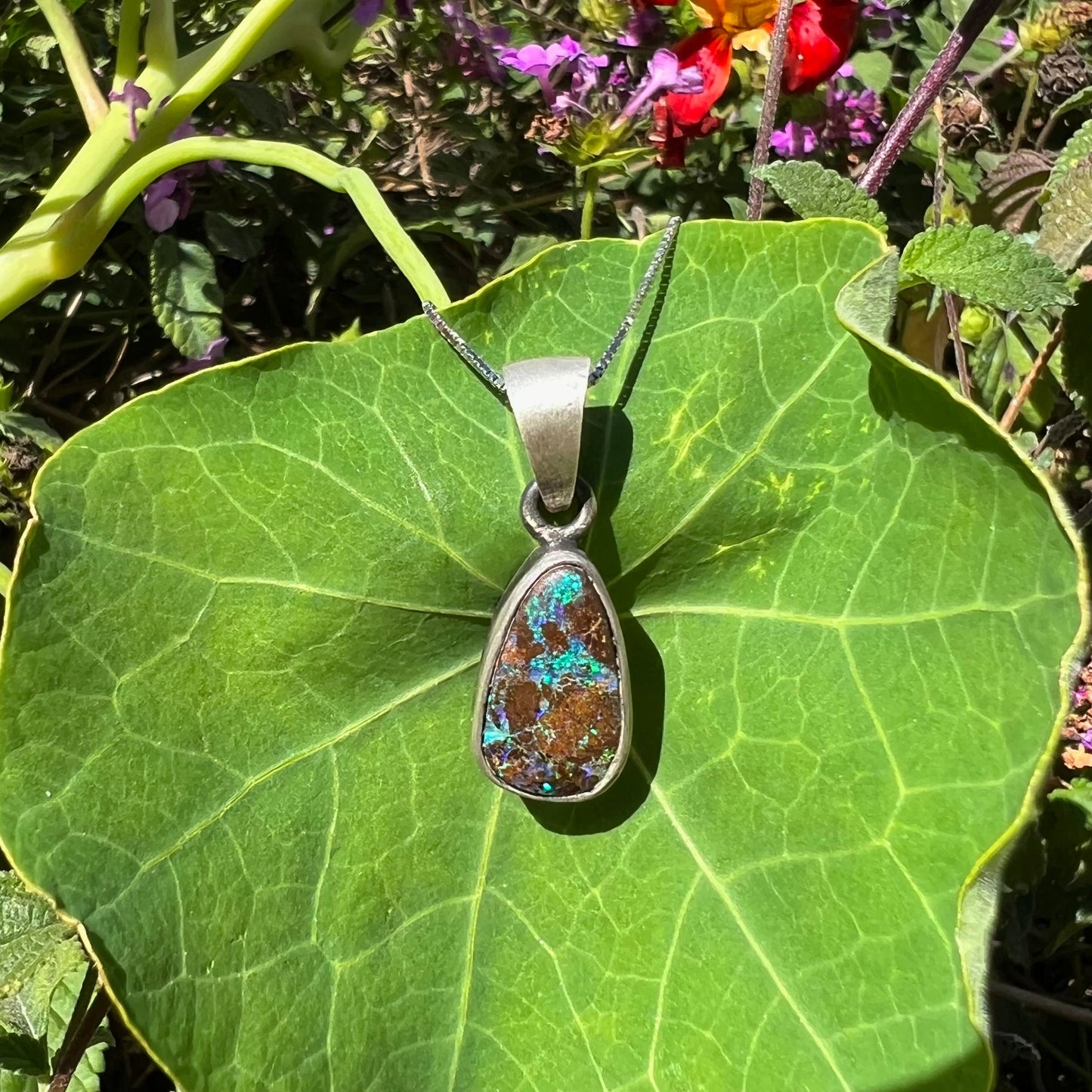 A handmade, satin finish sterling silver pendant set with a drop shaped boulder opal stone.