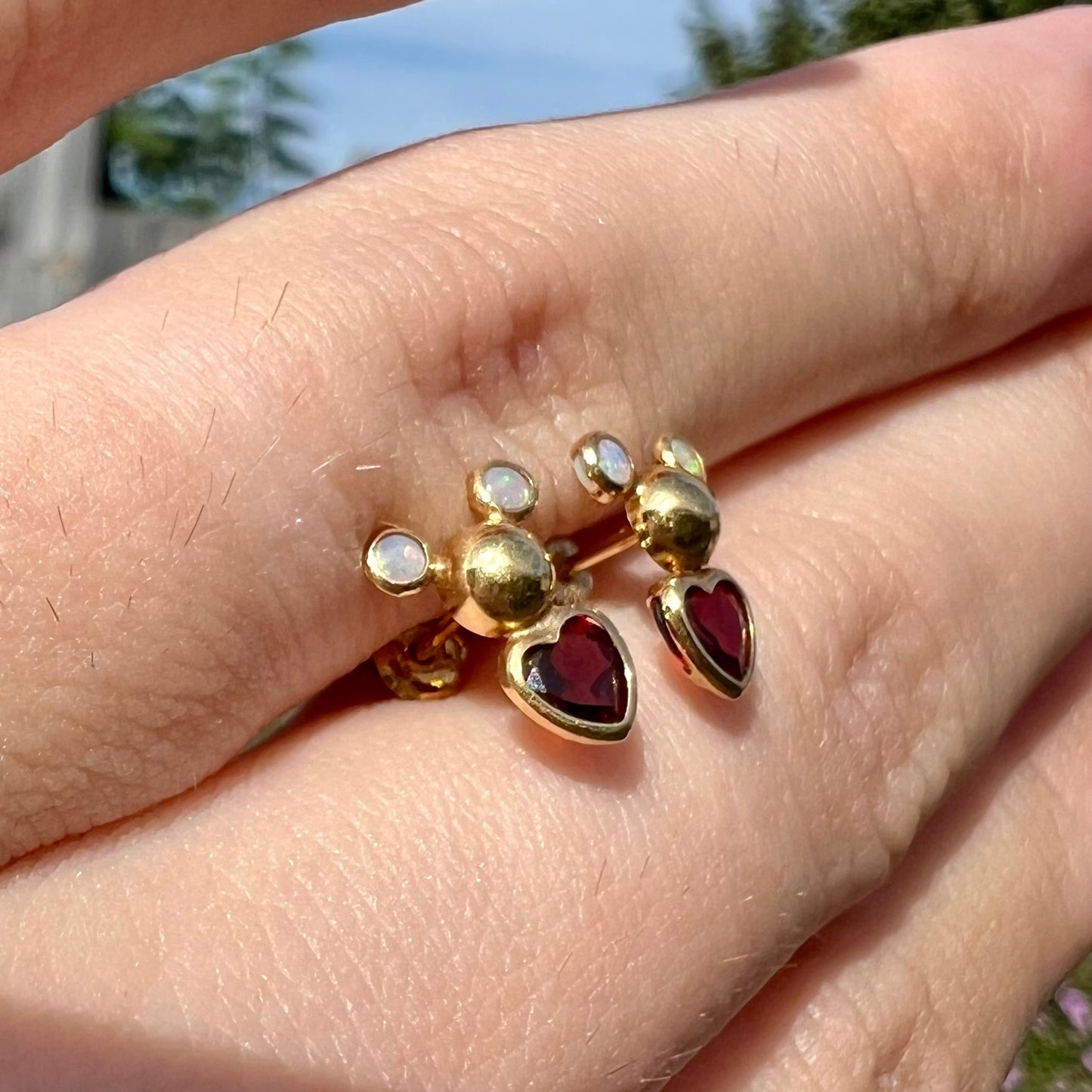 A pair of 18 karat yellow gold stud earrings set with two round fire opals and heart shaped garnets.