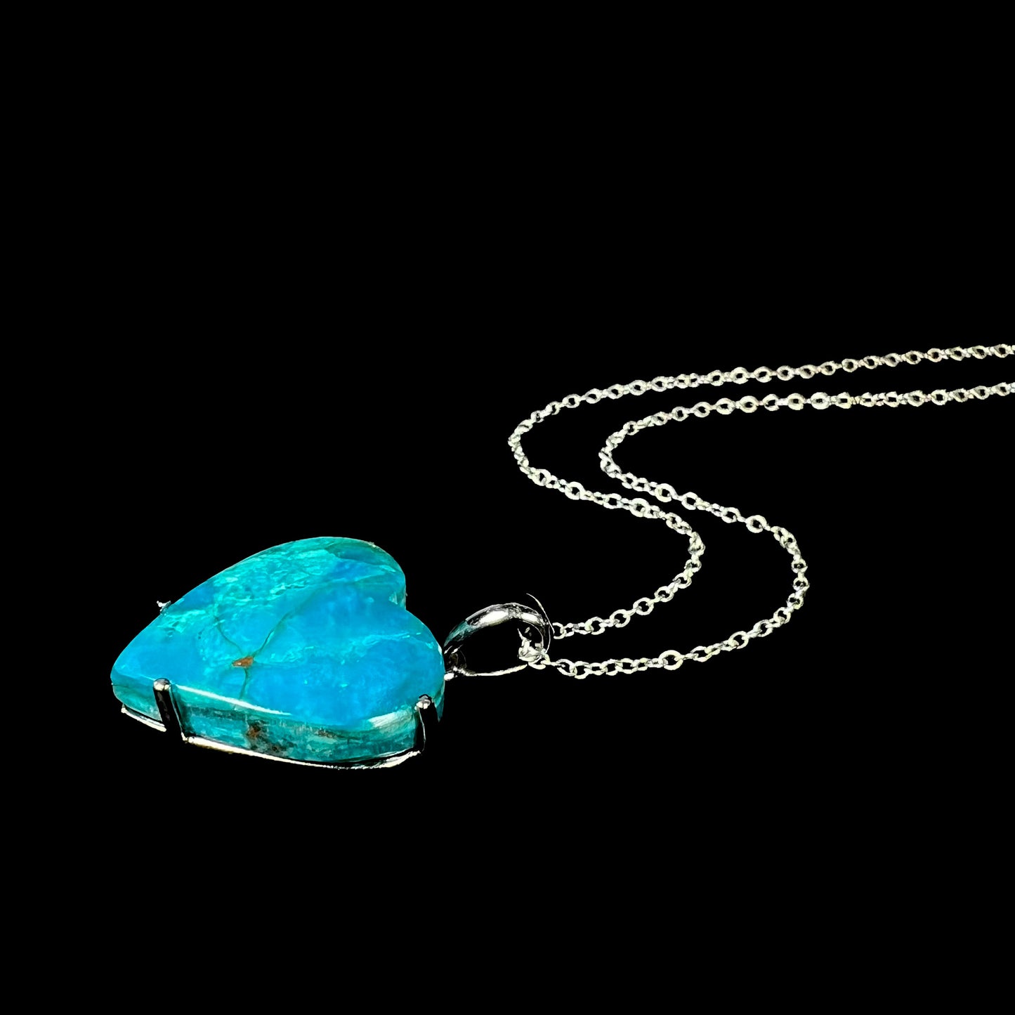 Angled view of a heart-shaped blue opal necklace resting against black background with visible matrix.
