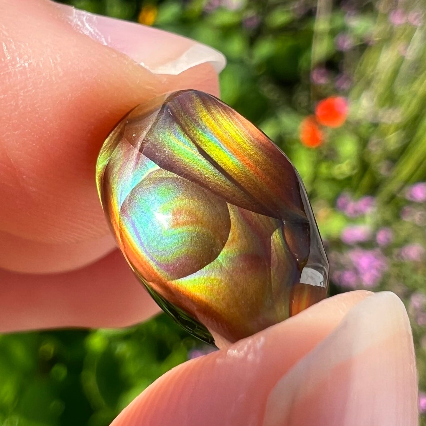 An oval cabochon cut Mexican fire agate stone.  The stone has bright, multicolored iridescent banding.