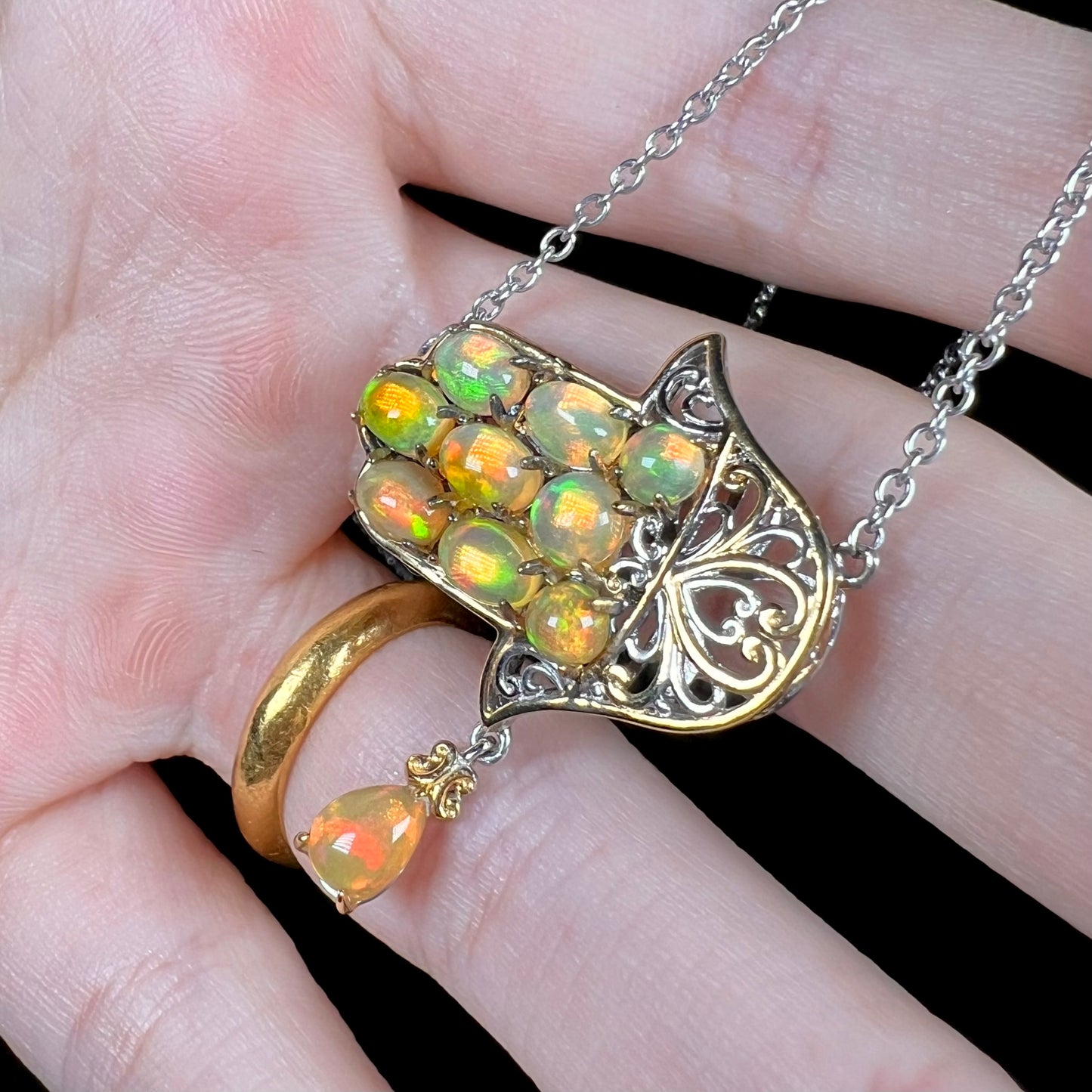 An Islamic opal hamsa necklace with filigree design, shown at an angle in a hand.
