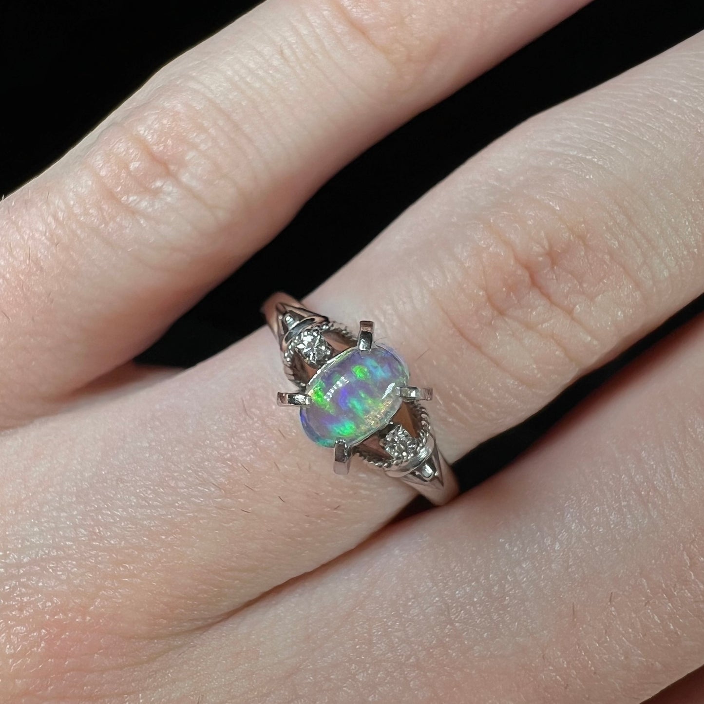 A green jelly opal and diamond engagement ring on a finger. The ring has two diamond accents.